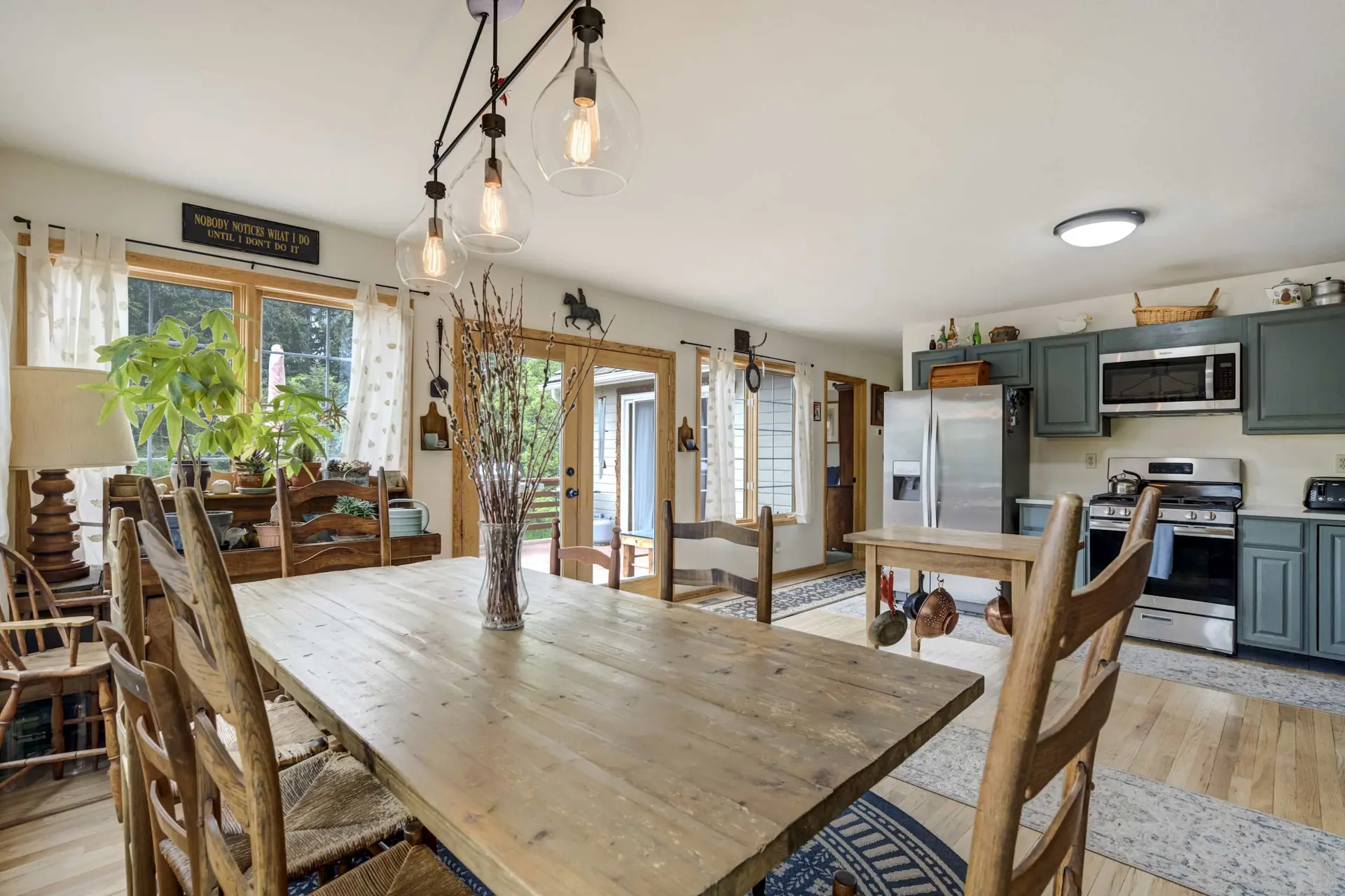 Rustic dining room and kitchen with a large wooden table, teal cabinets, and a sign on the wall.