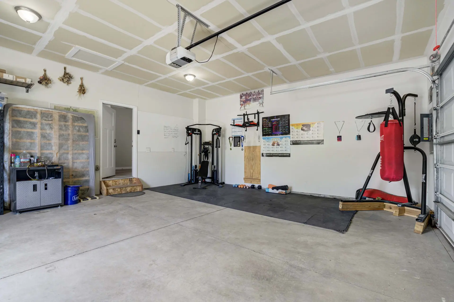 A well-lit garage converted into a home gym with exercise equipment, storage, and concrete floor.