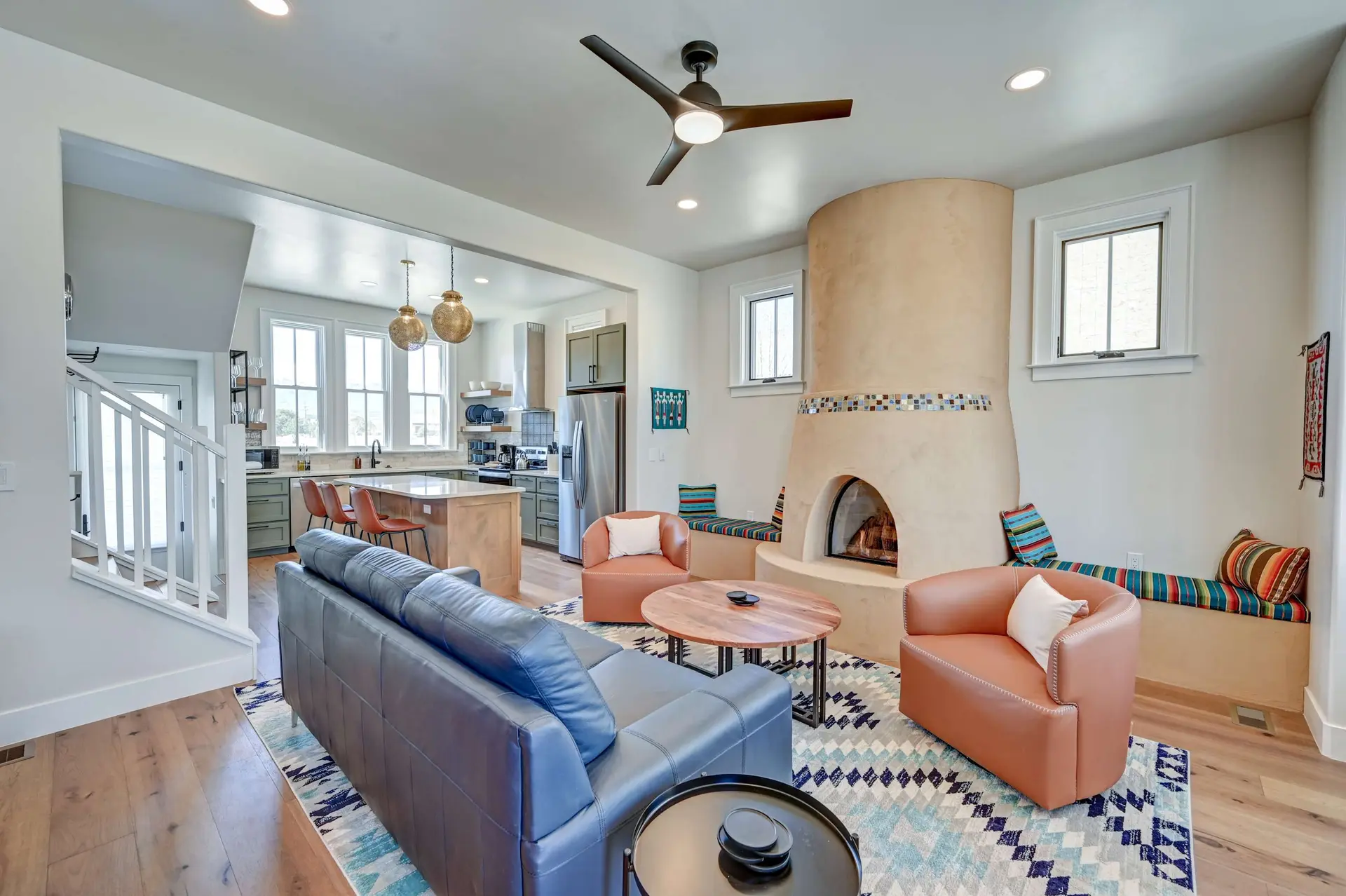 Modern living room with a fireplace, sofa, chairs, and an open-concept kitchen.