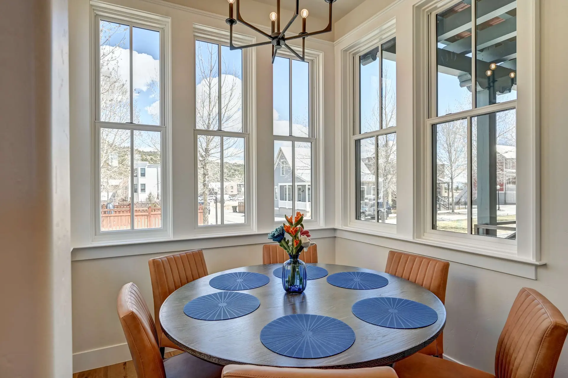 A round dining table with six blue placemats and a vase of flowers.
