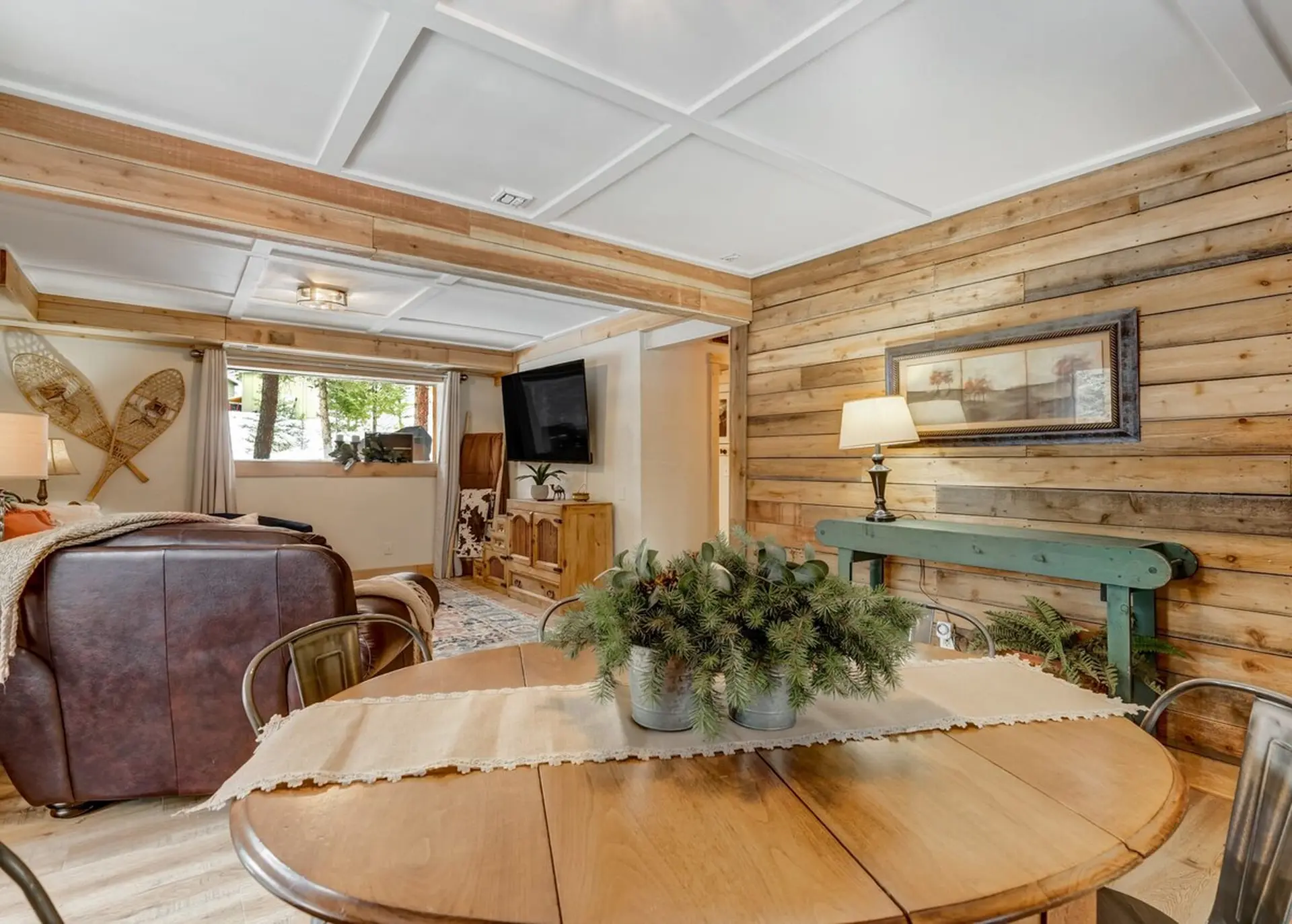Rustic living/dining room with wood paneling, coffered ceiling, leather armchair, and dining table.