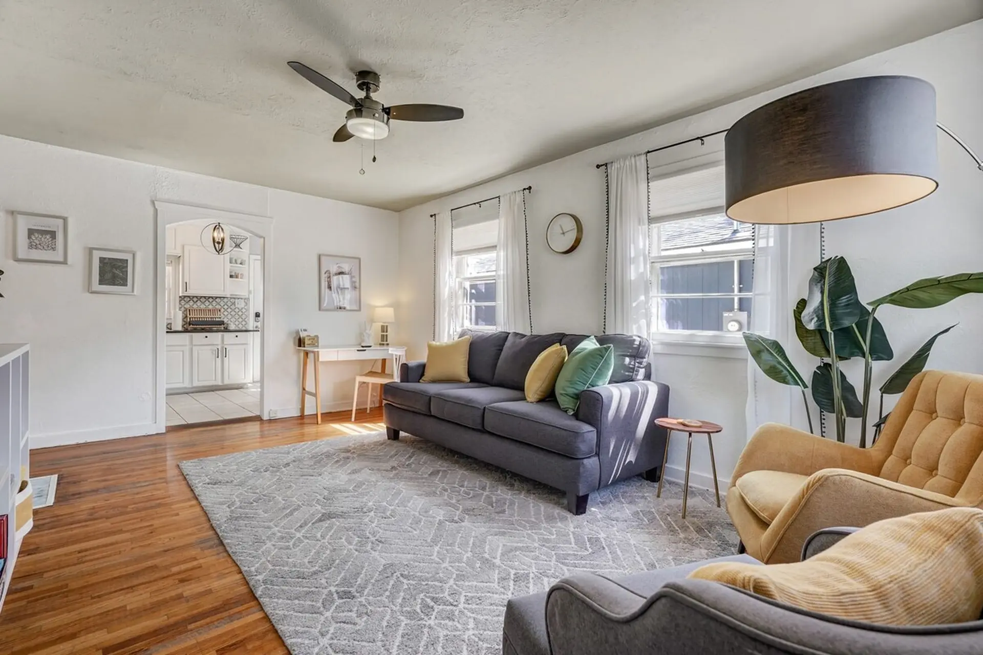 A welcoming living room featuring a gray sofa, armchairs, a large patterned rug, and a kitchen archw