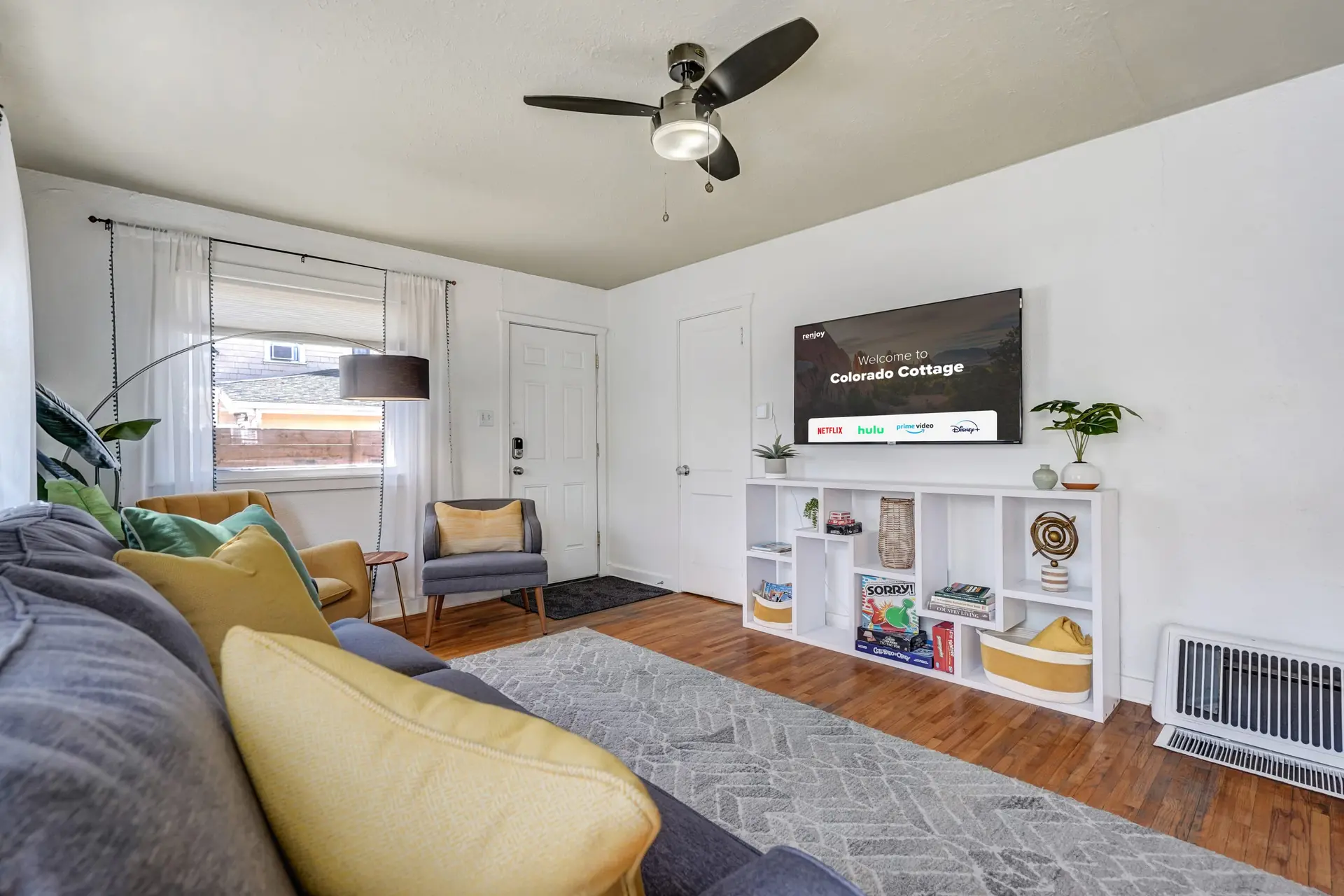 A bright and cozy living room with a blue couch, yellow armchairs, a TV, and a patterned rug.
