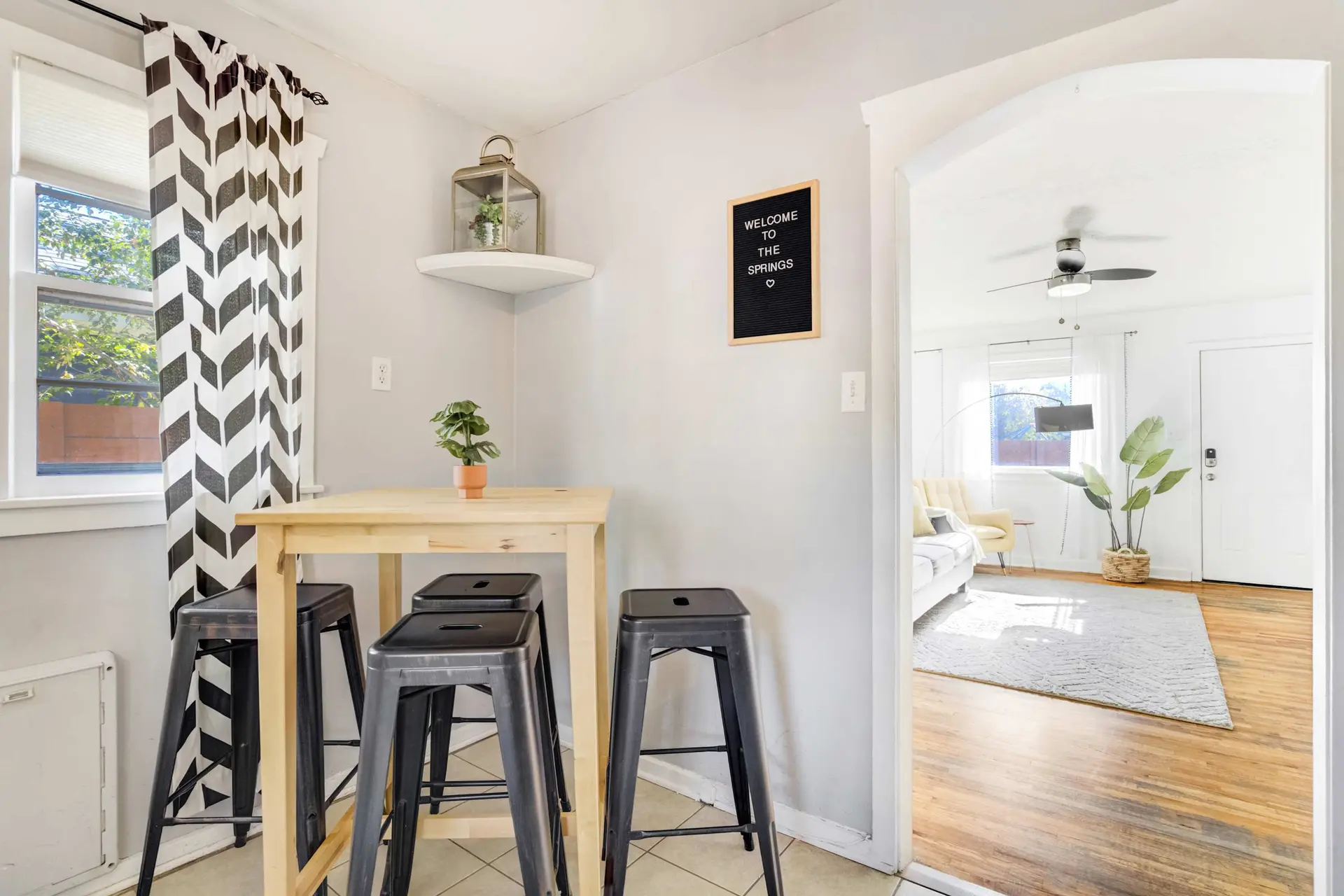 A small dining area with a table and stools, adjacent to a living room with a couch.