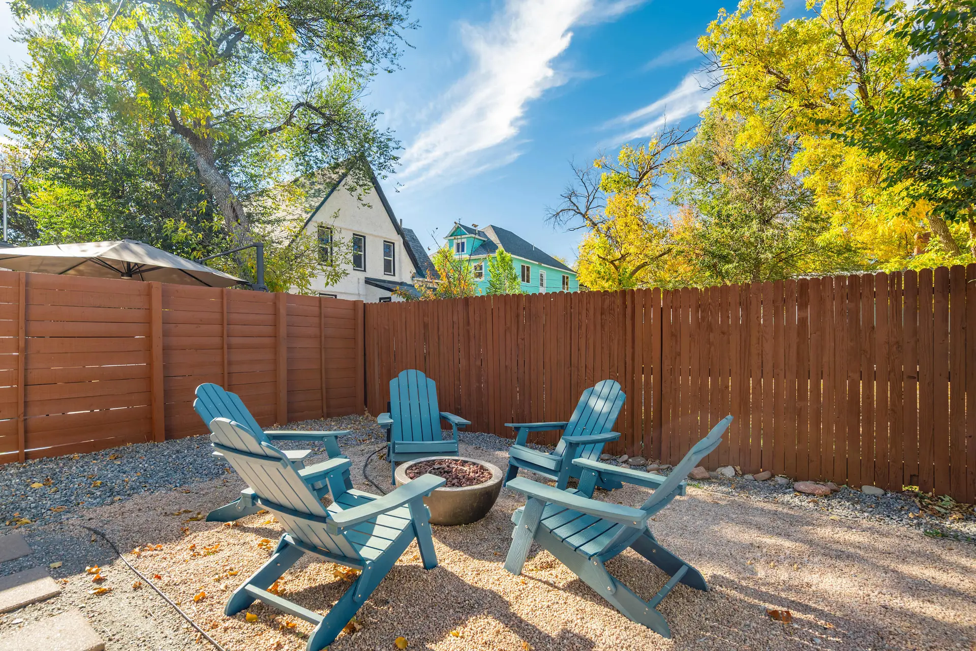A backyard patio with a fire pit, teal chairs, and a wooden fence.
