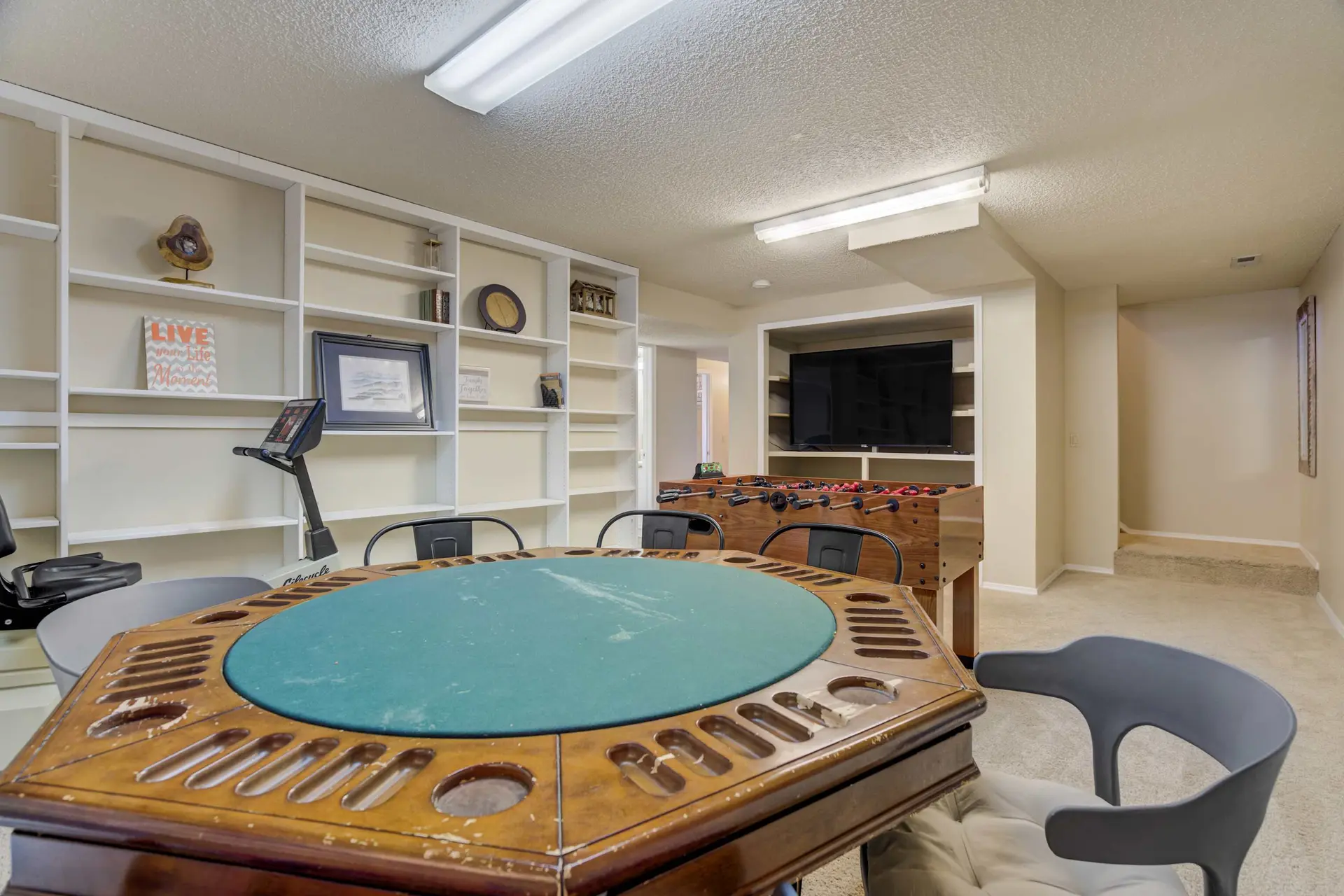 A game room with a poker table, foosball table, and treadmill.