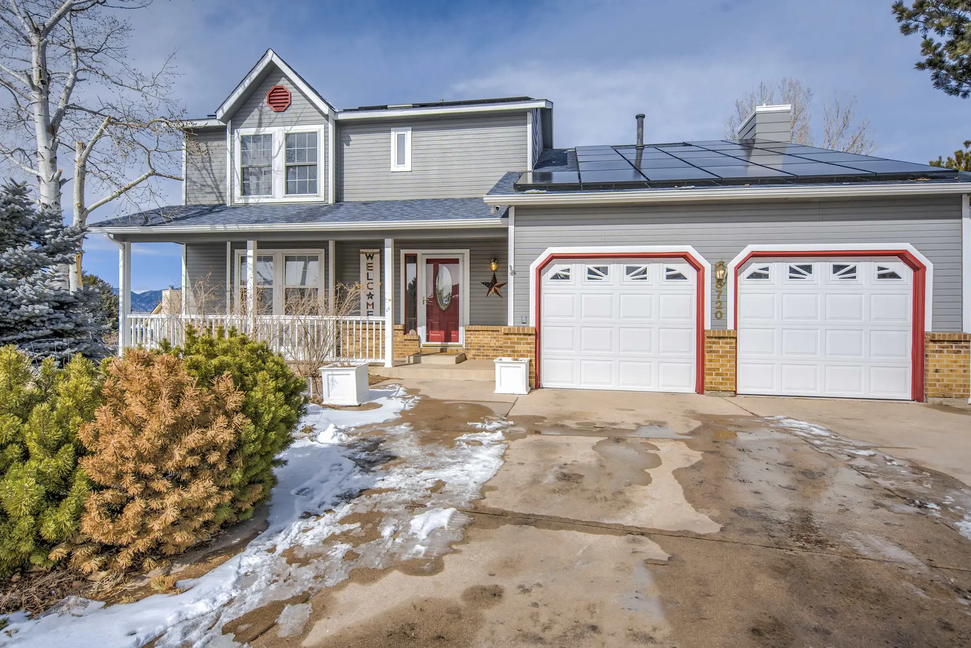 A two-story house with a grey exterior, red garage doors, and solar panels on the roof.