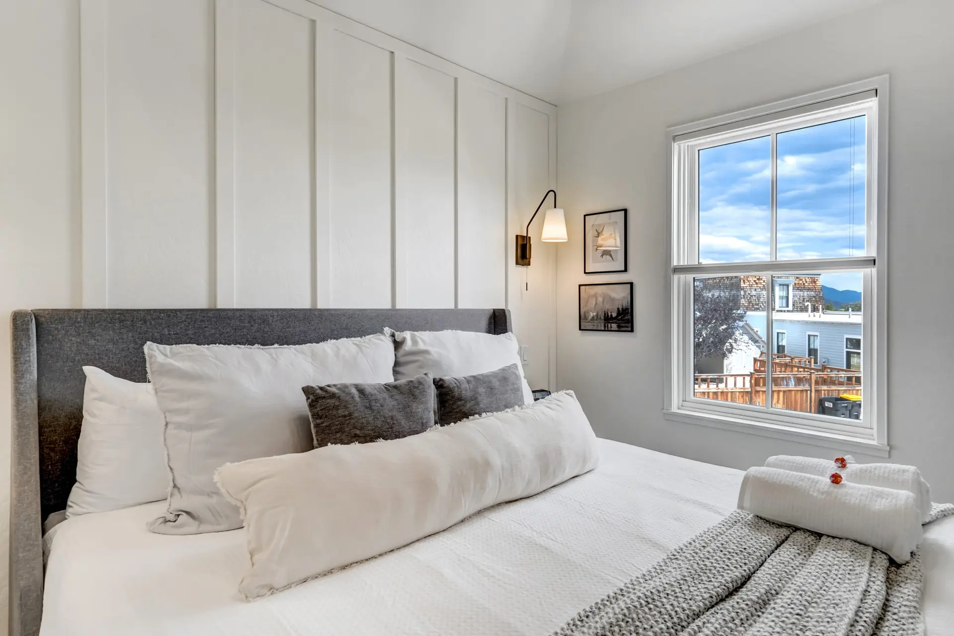 A bright bedroom with a bed featuring a gray upholstered headboard and white and gray pillows.