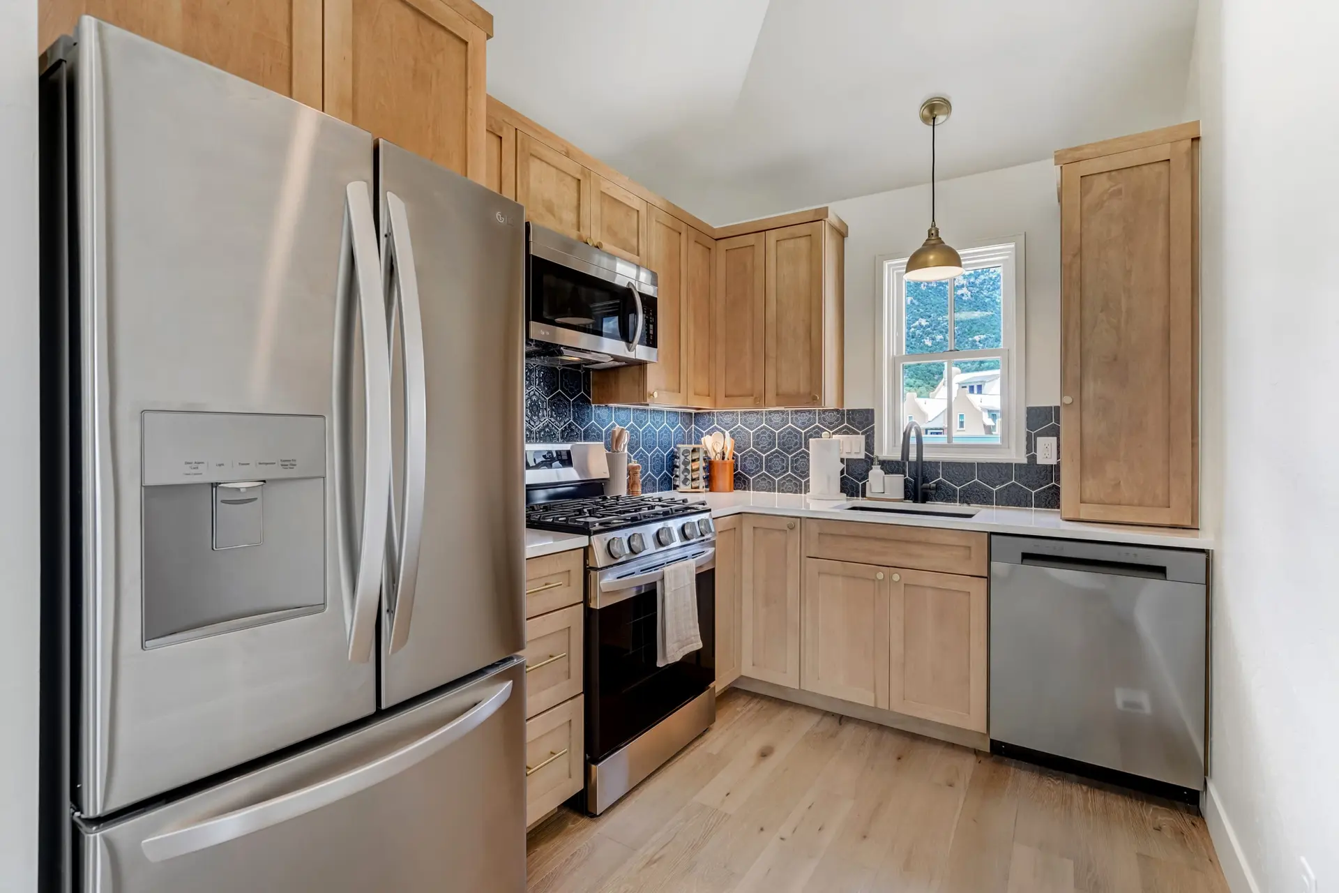 A contemporary kitchen with stainless steel appliances, light wood cabinets, a blue tile backsplash,