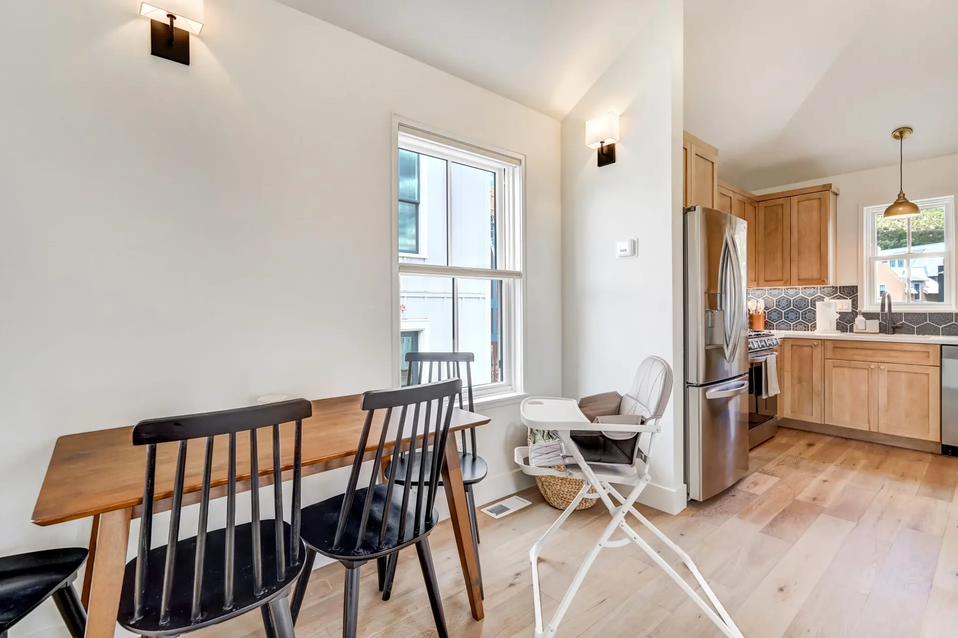 A dining table and chairs are in a kitchen with wood cabinets and a stainless steel refrigerator.