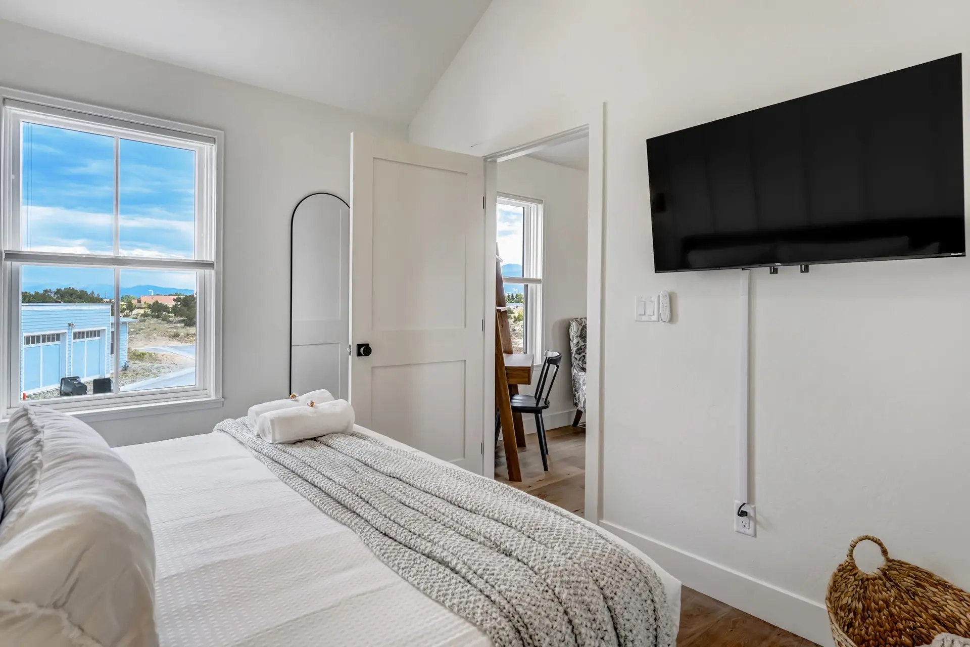 A white bedroom with a tv, bed, and a view of a garage and mountains.