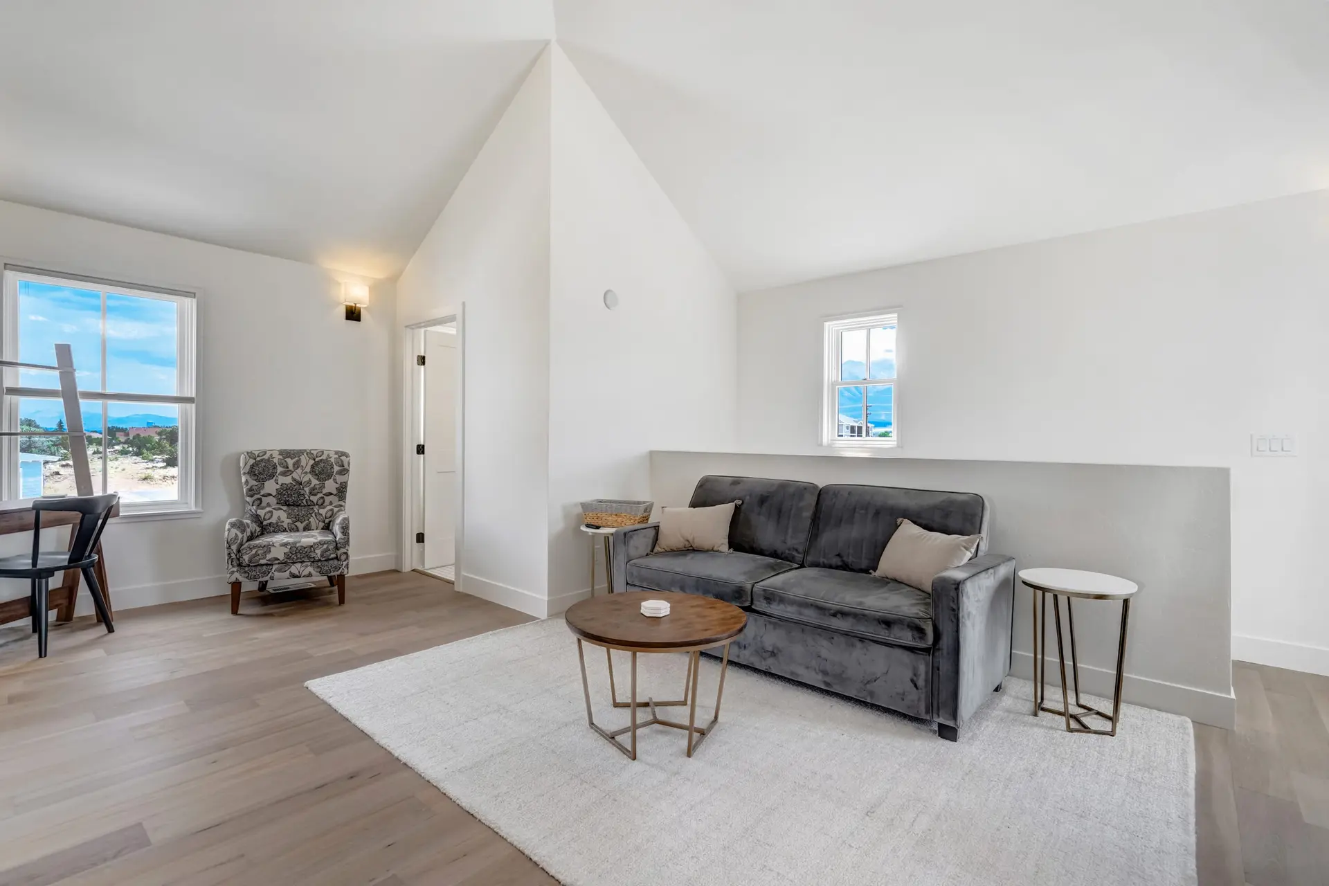 A gray sofa with decorative pillows sits on a white rug in a bright room.