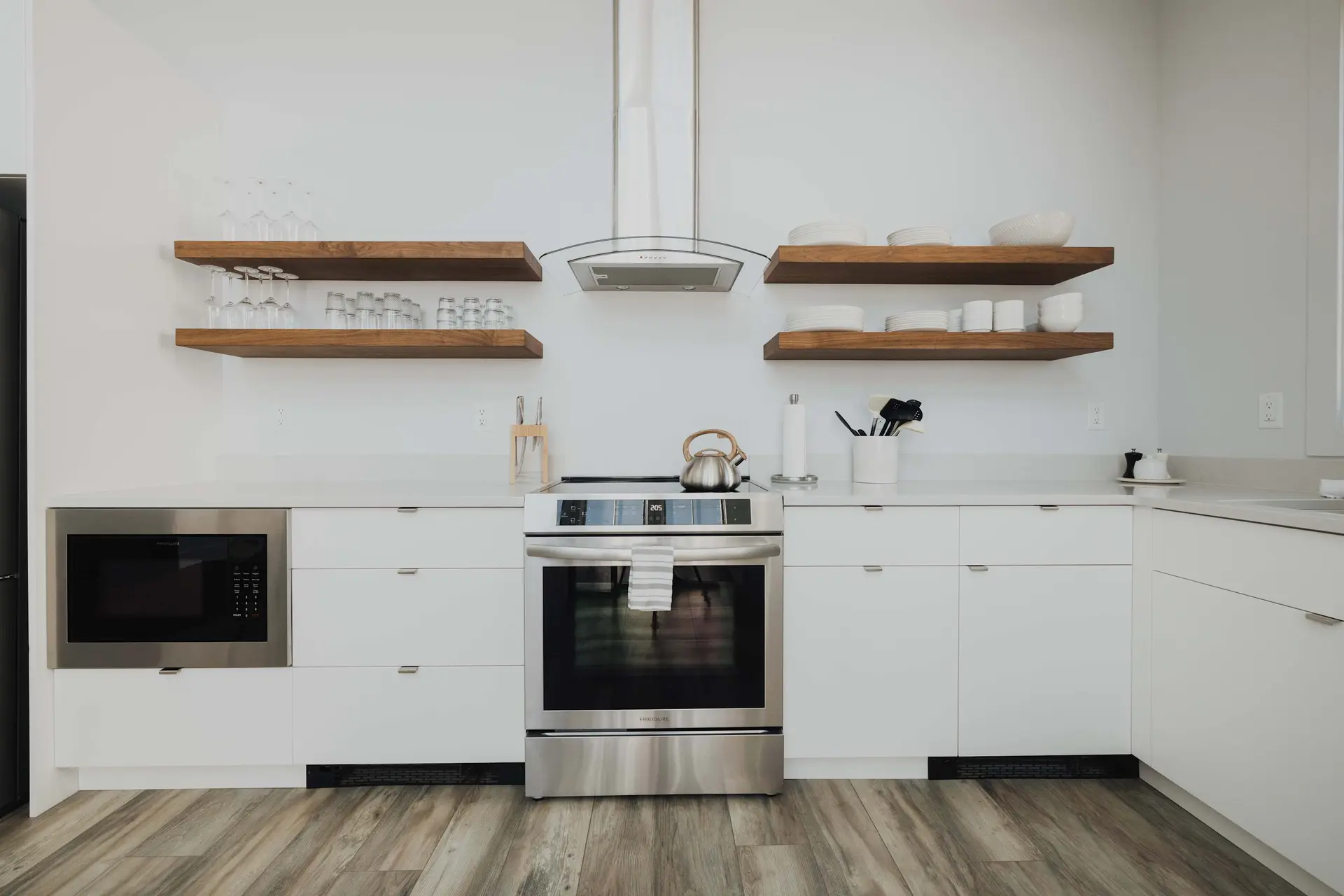 A modern kitchen with white cabinets, wooden shelves, and stainless steel appliances.