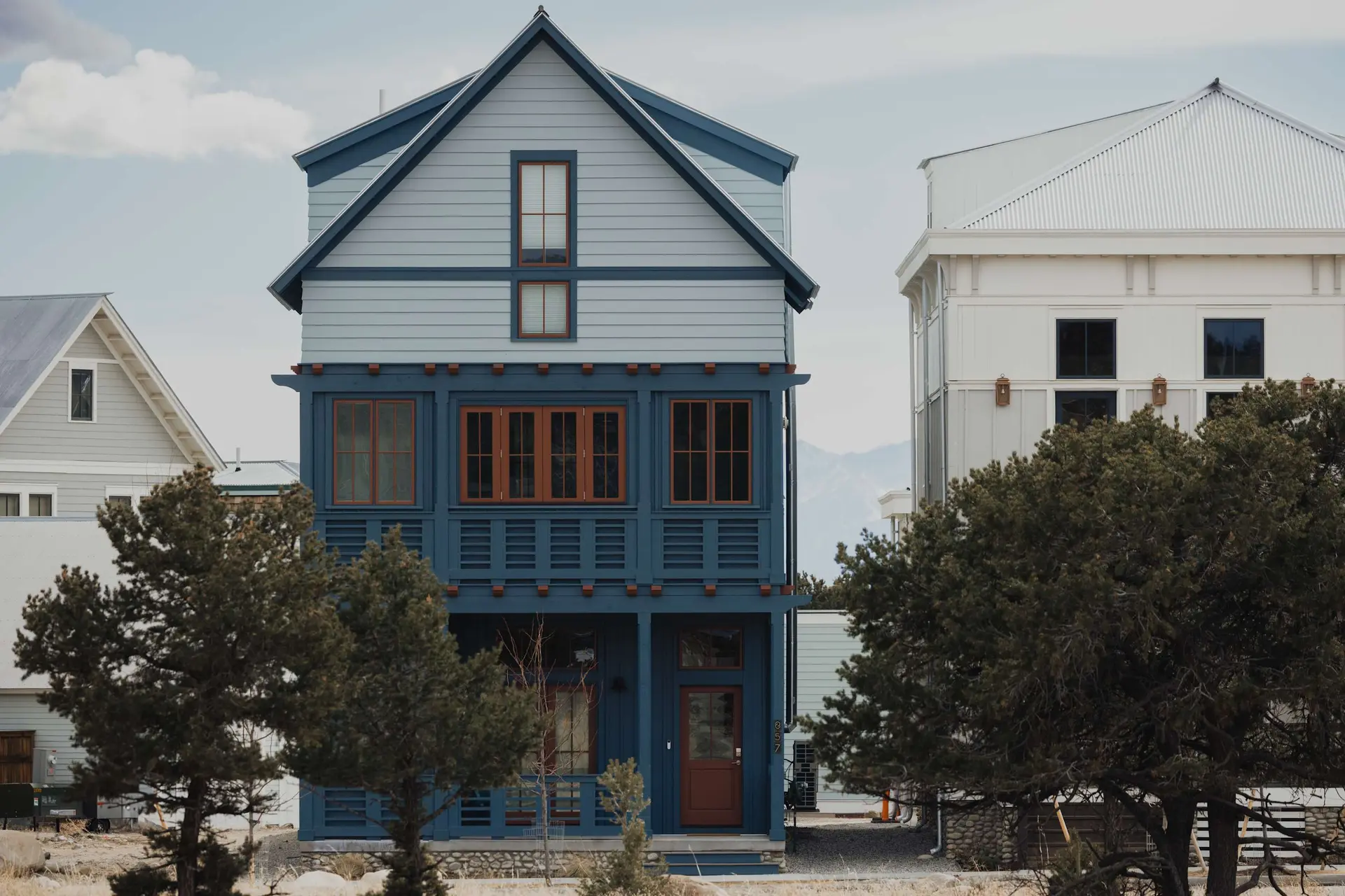 A tall, narrow blue house with a brown door is in front of a white building.
