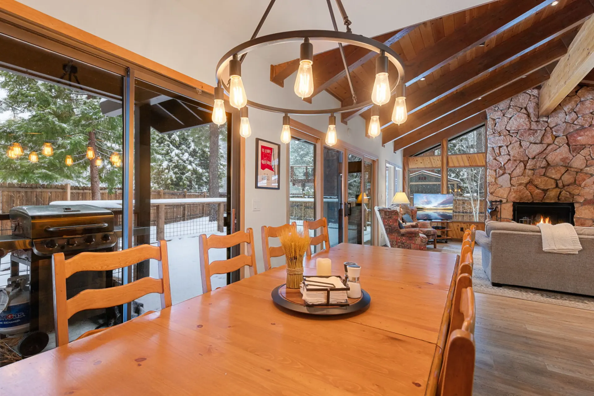 A wooden dining table and chairs are in the foreground, with a fireplace and seating area in the bac