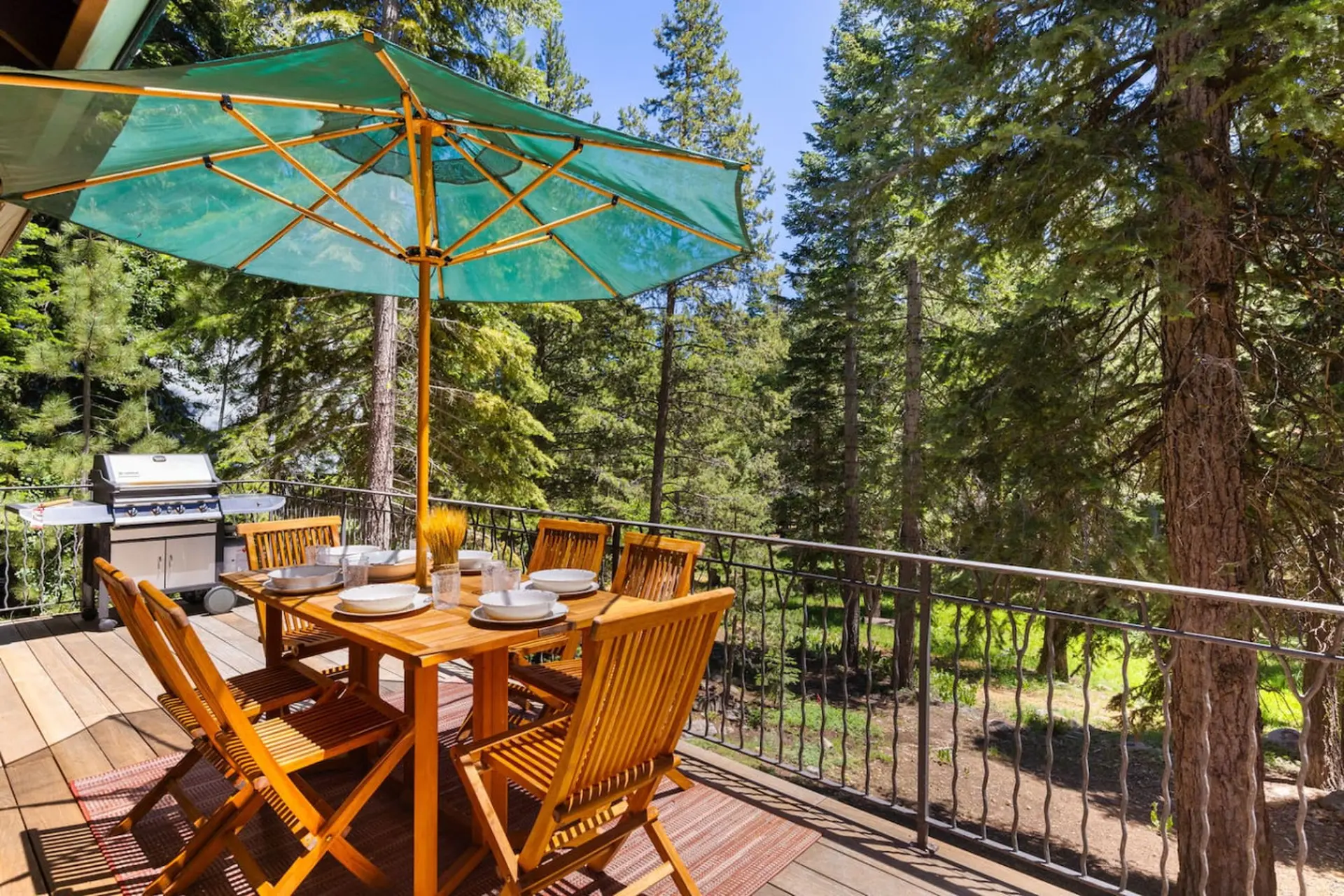 Outdoor dining table with chairs and umbrella on a wooden deck surrounded by trees.
