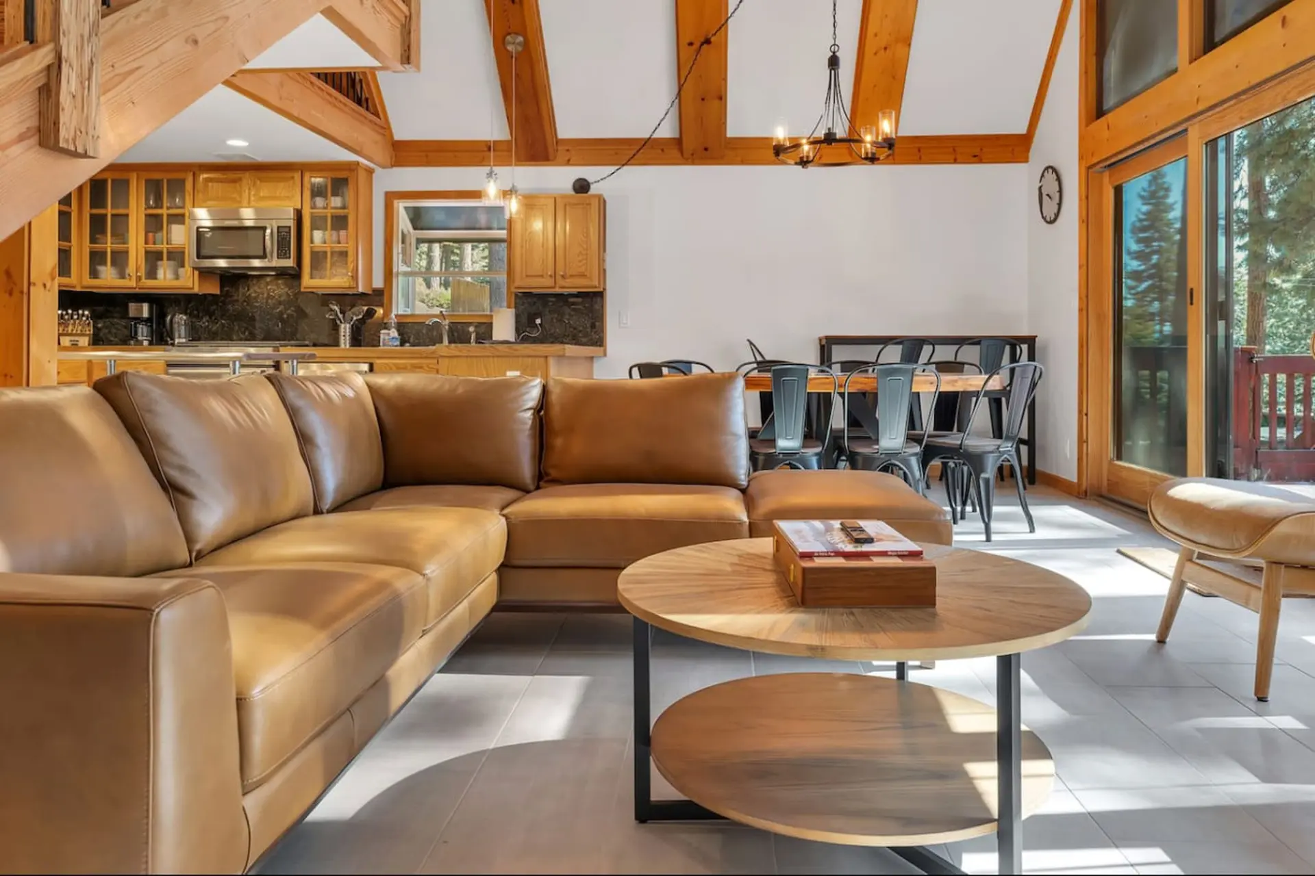 A spacious, open-plan living area with a large leather sectional, dining table, and wood beams.