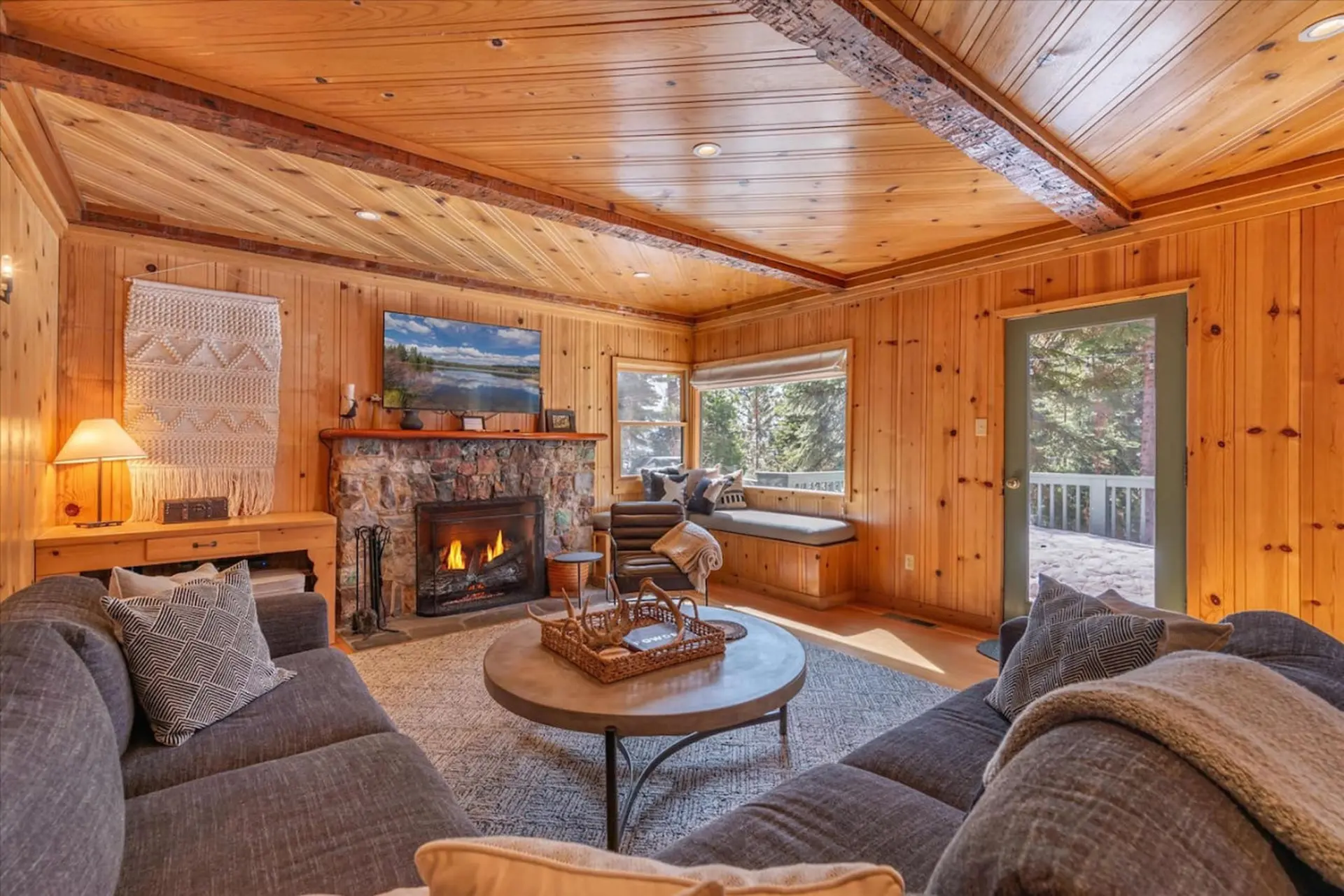 Cozy cabin living room with fireplace, TV, and large window seat.