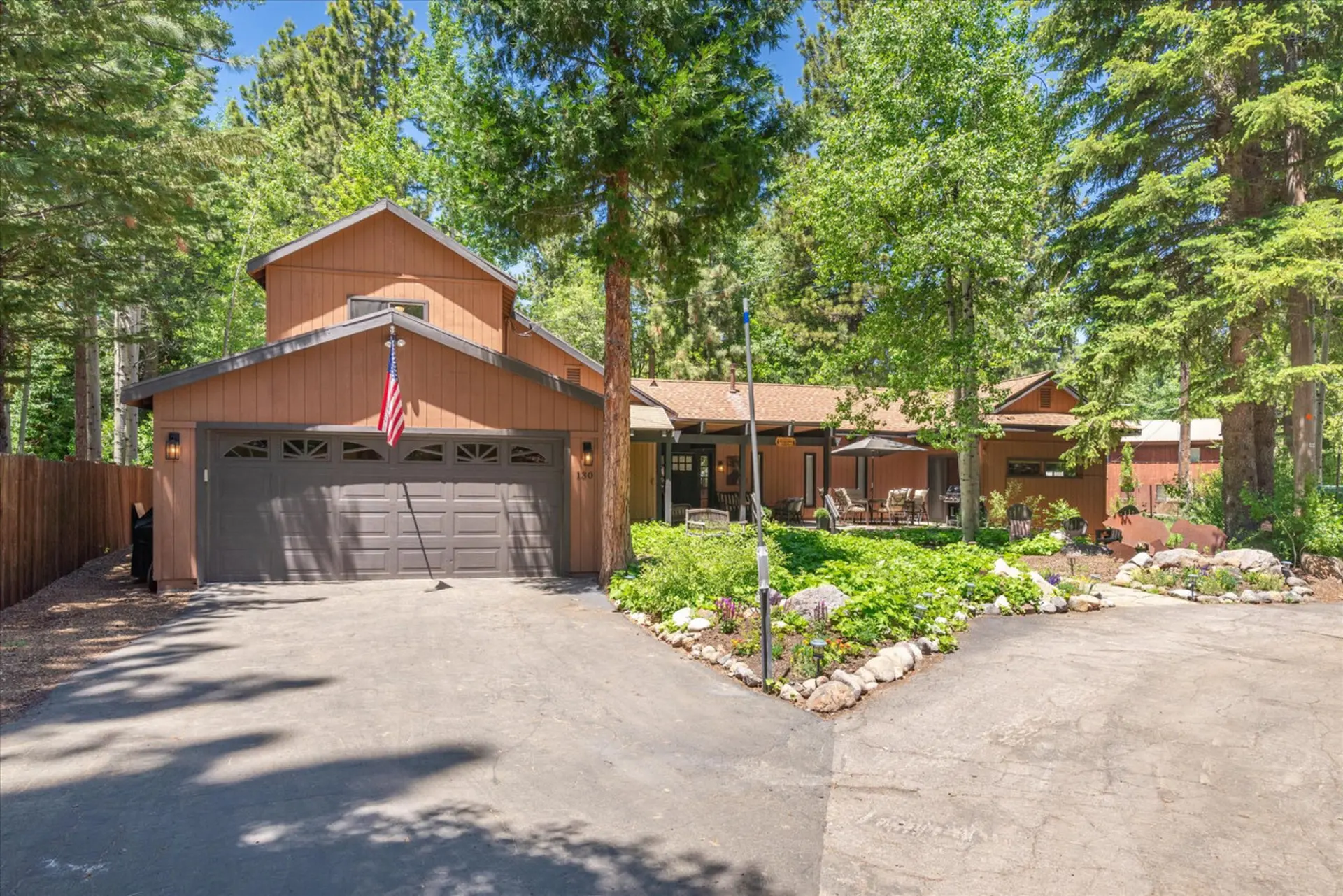 A brown house with a garage and an American flag in front of trees.
