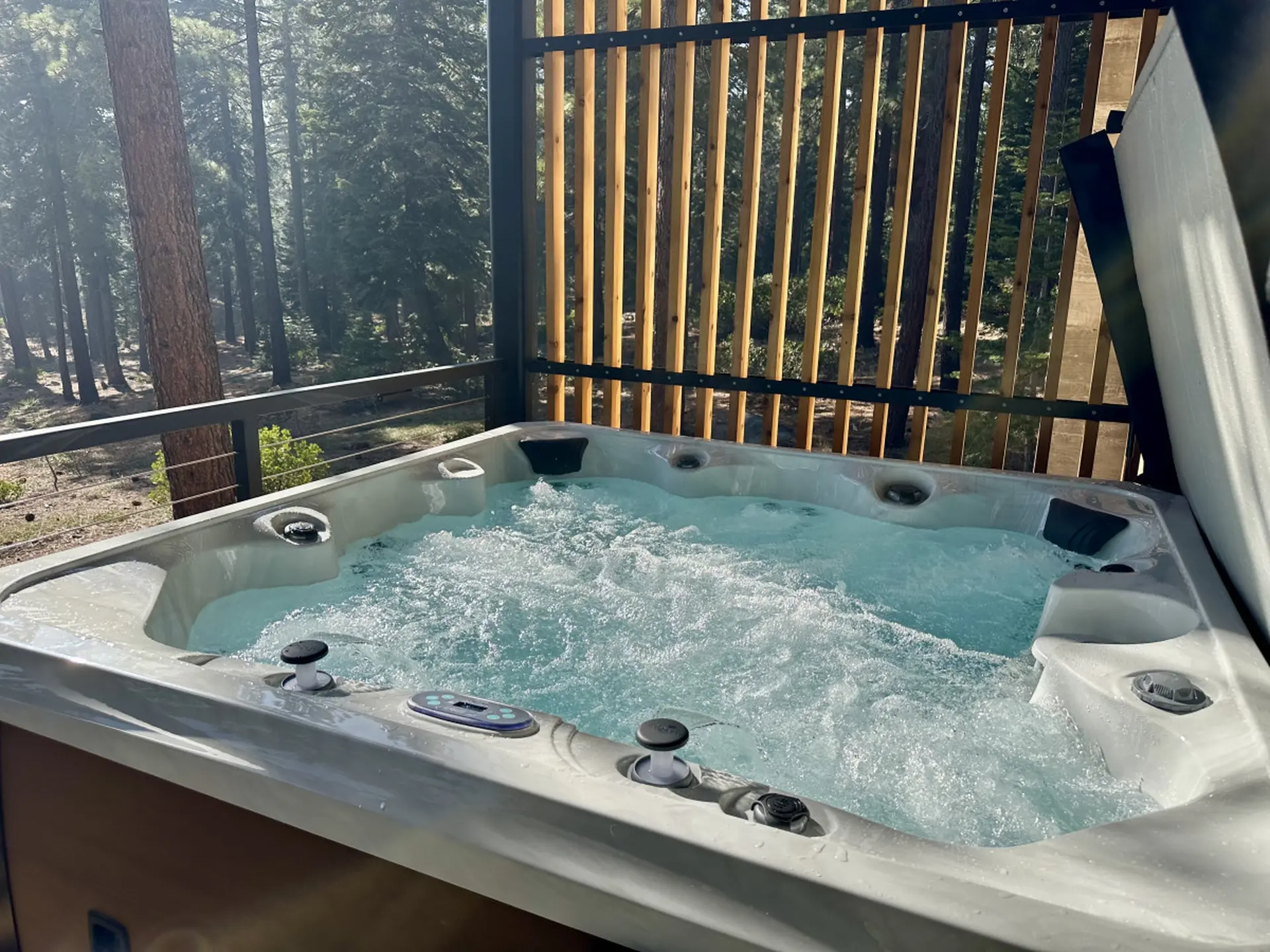 A bubbly hot tub sits on a deck surrounded by trees in a forest.