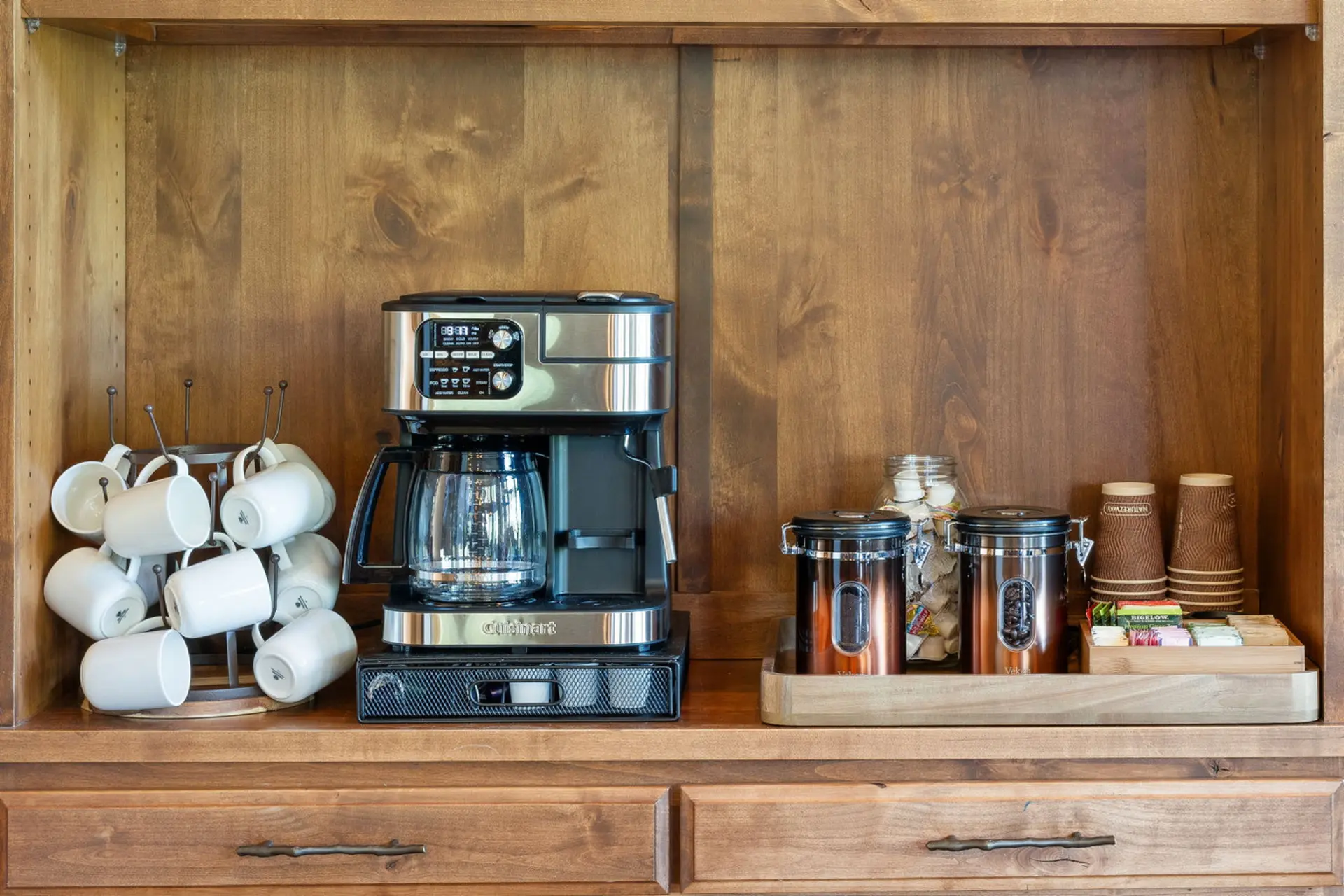 A coffee station with a Cuisinart coffee maker, mugs, coffee canisters, and disposable cups.