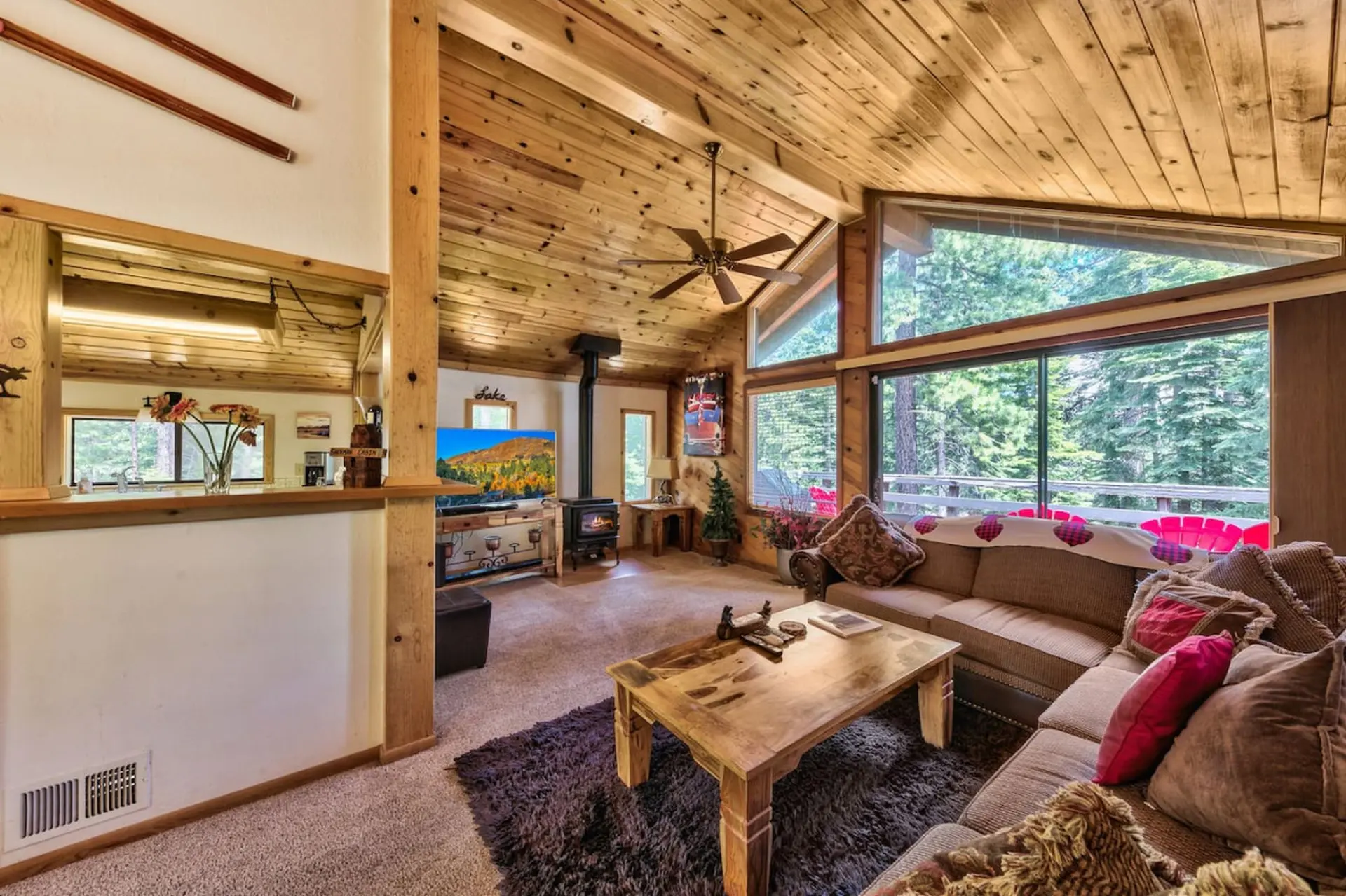 Cozy living room with wood paneled walls and ceiling, large windows, and fireplace.