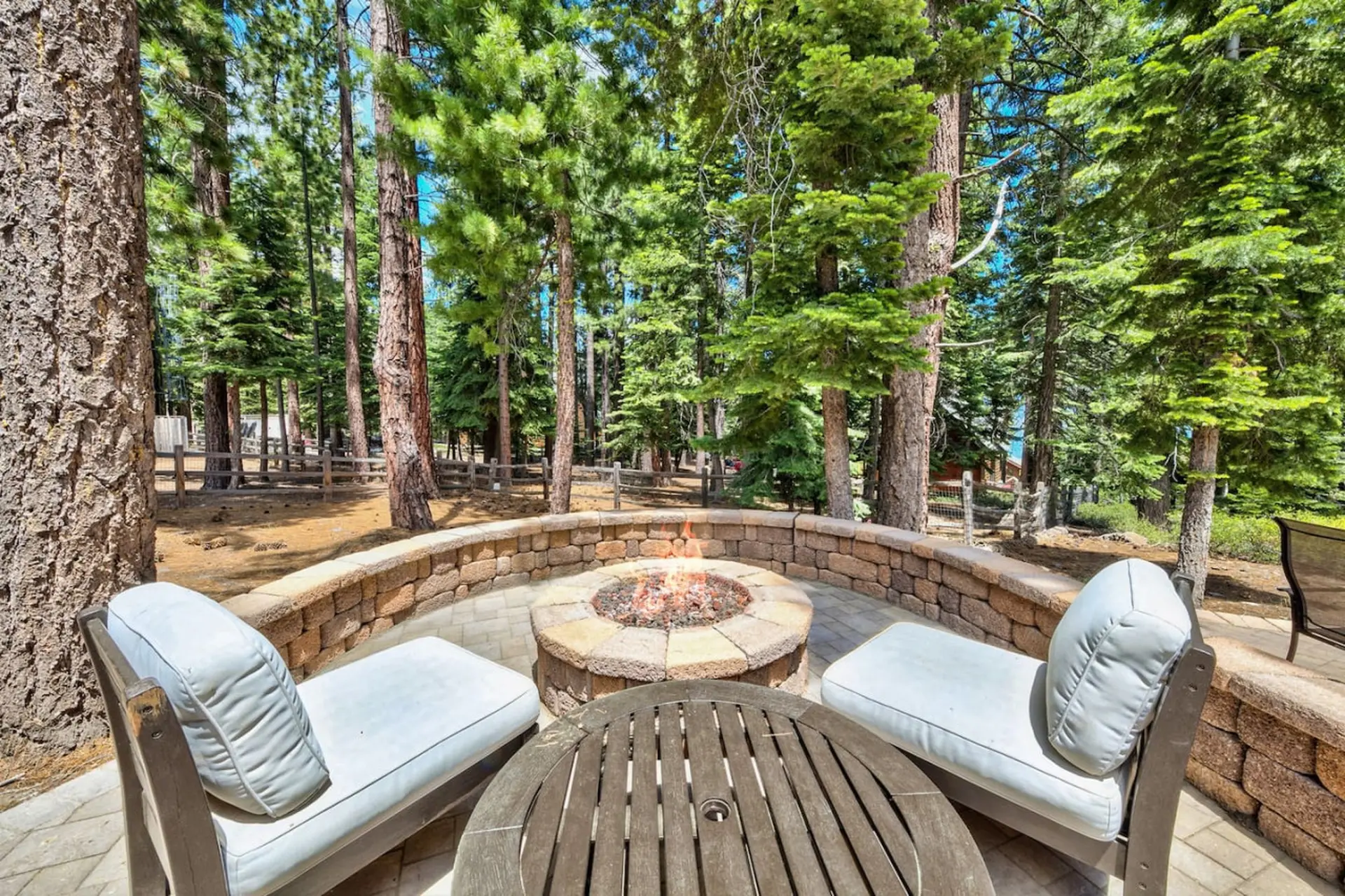 Outdoor fire pit surrounded by chairs and trees.