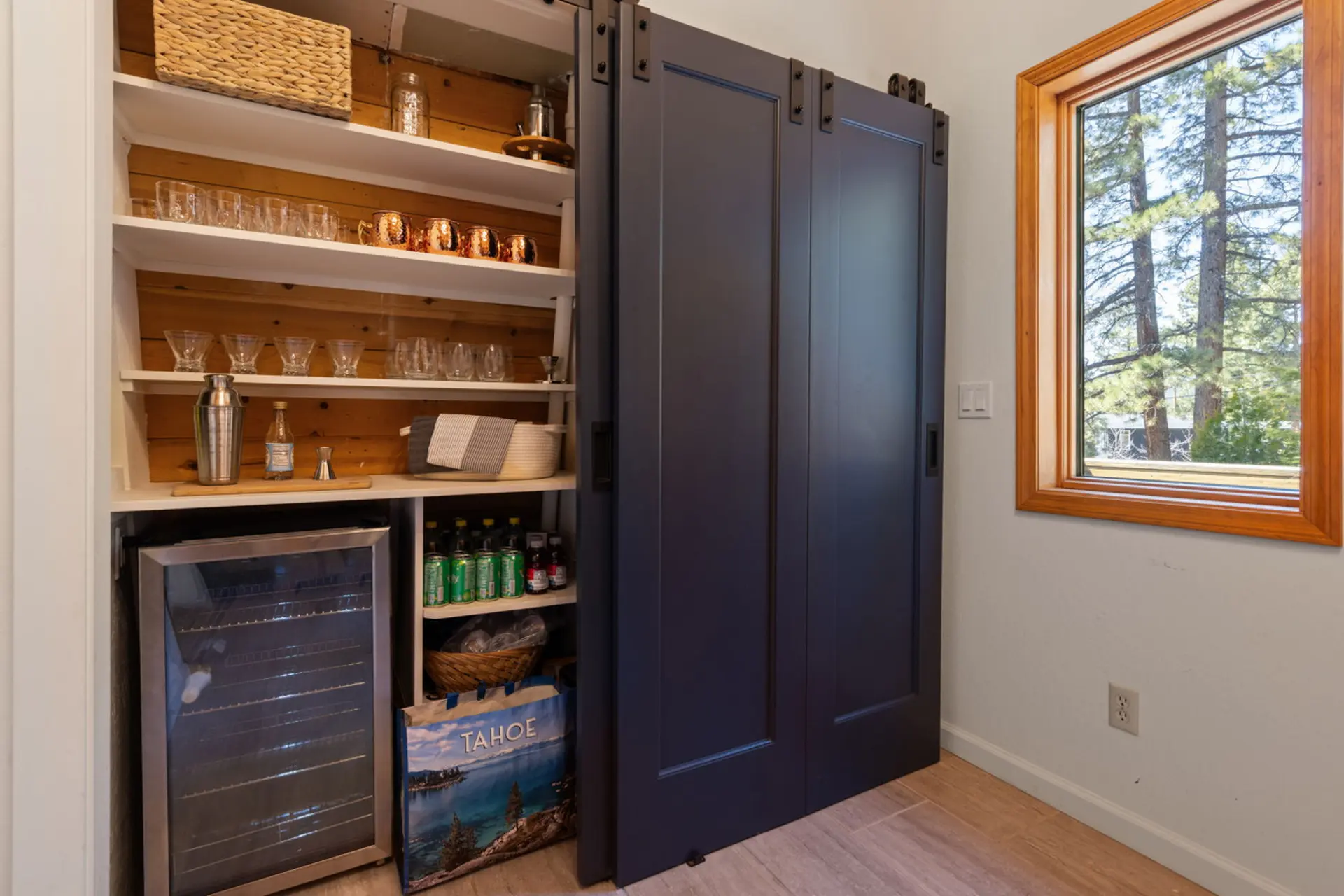 A bar area with a cooler, drinks, glassware, and sliding doors.