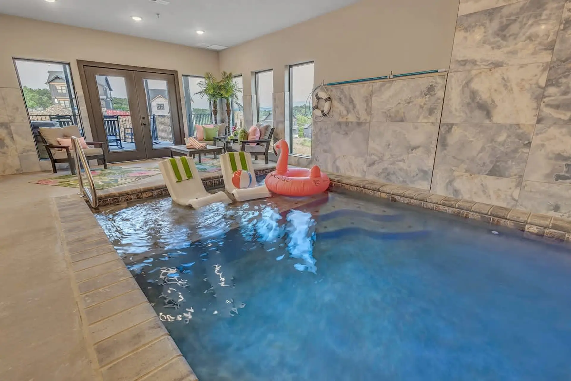 An indoor pool area with lounge chairs, a flamingo float, and a beach ball.
