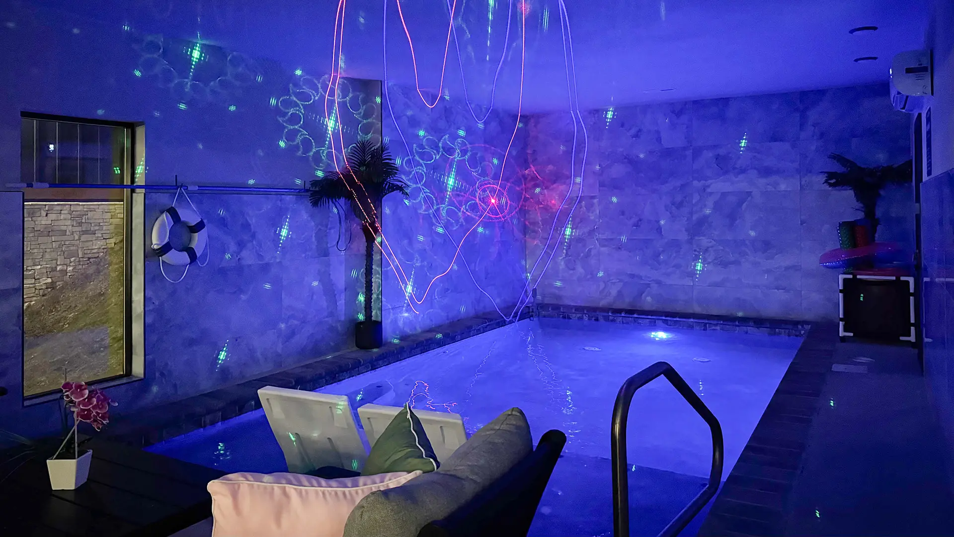 An indoor pool with blue lighting, laser lights, and lounge chairs.