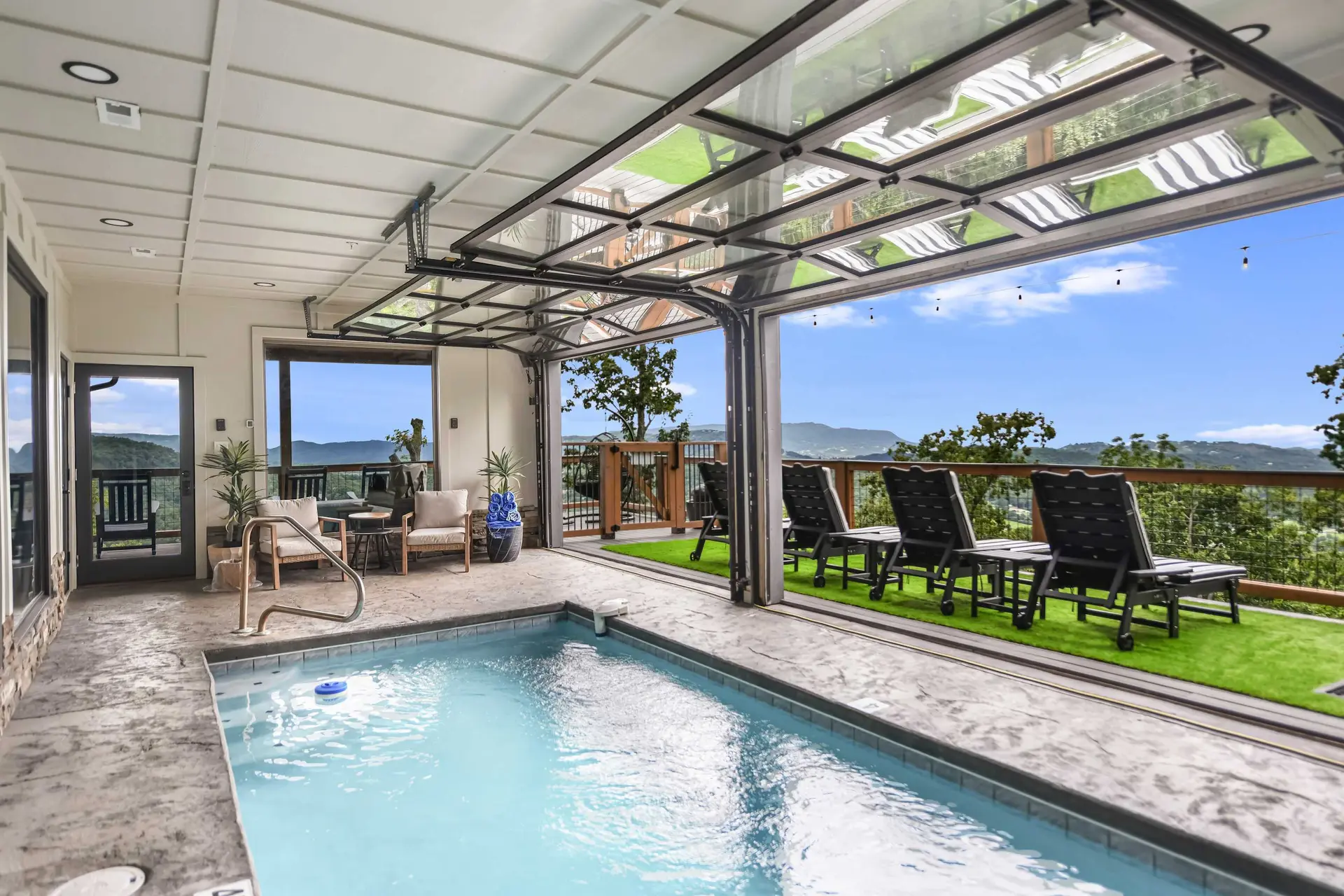Indoor pool with a retractable glass wall opening to a deck and mountain views.