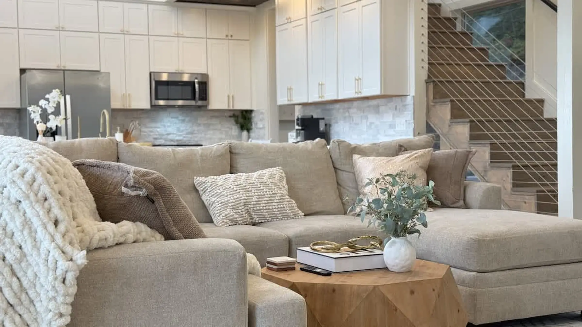 A sectional sofa sits in front of a kitchen, with a wooden coffee table in the foreground.