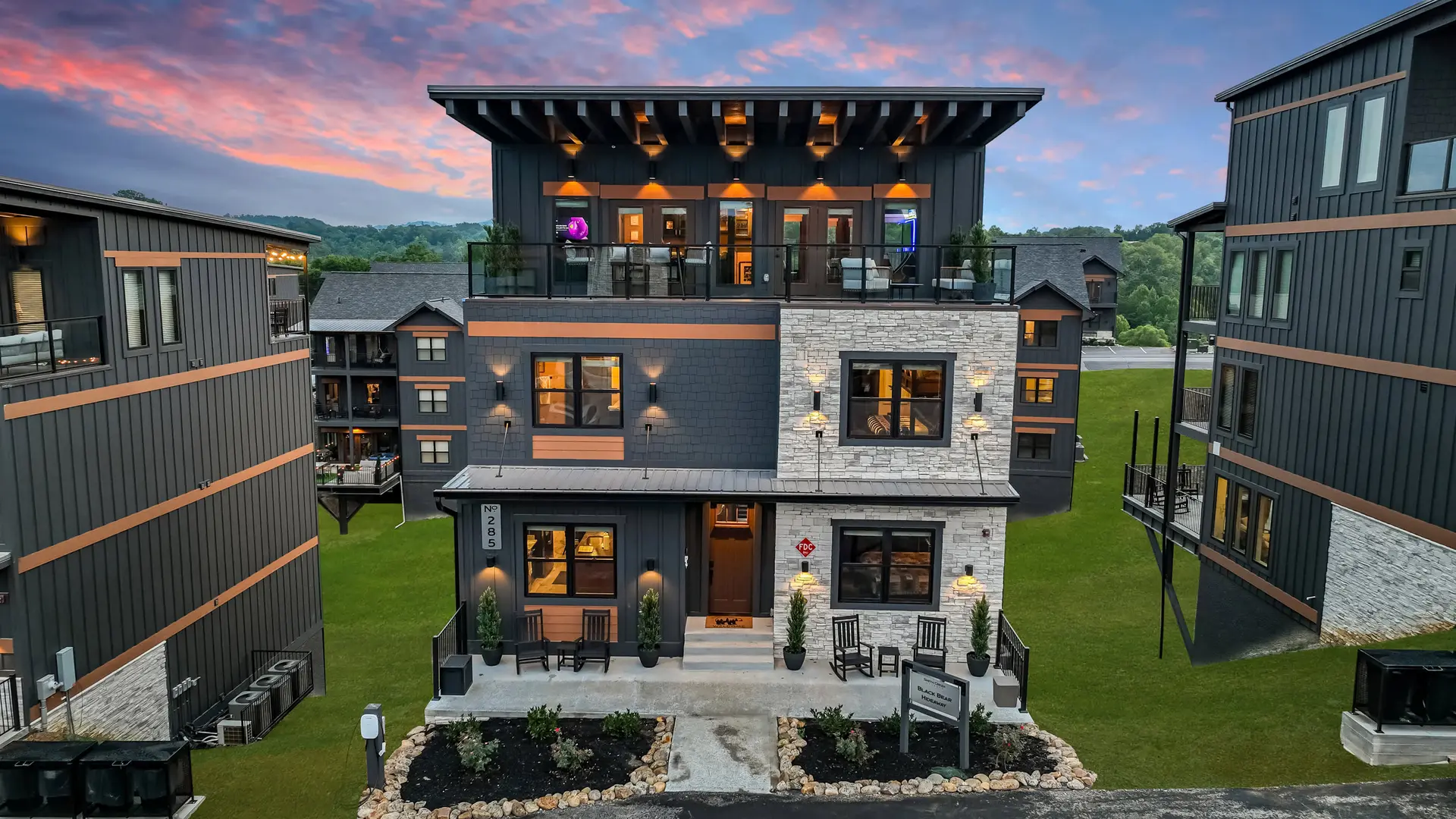 Modern luxury cabin with stone accents and balconies, set against a colorful sunset sky.