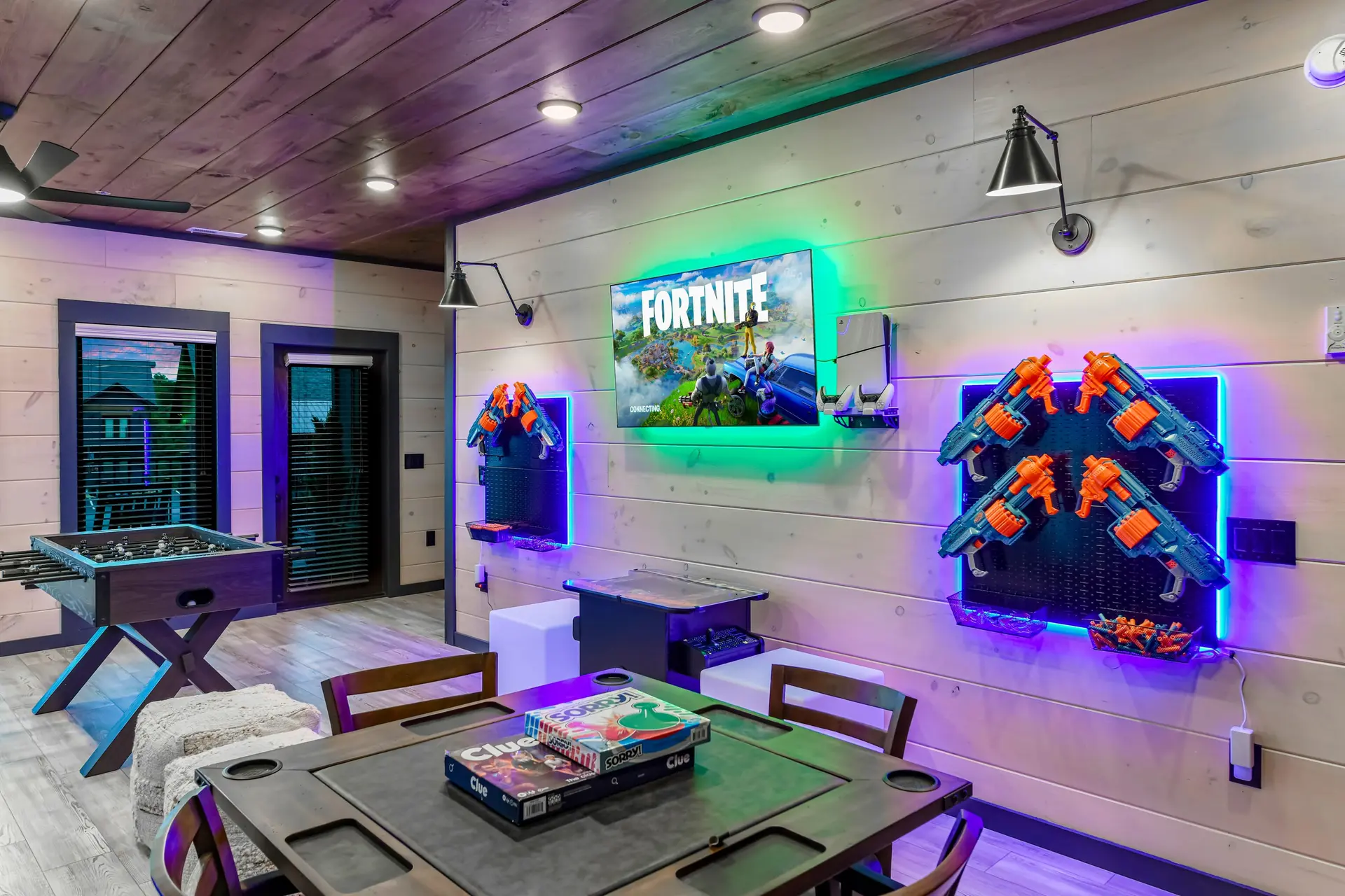 A room with a foosball table, game consoles, and dart guns.