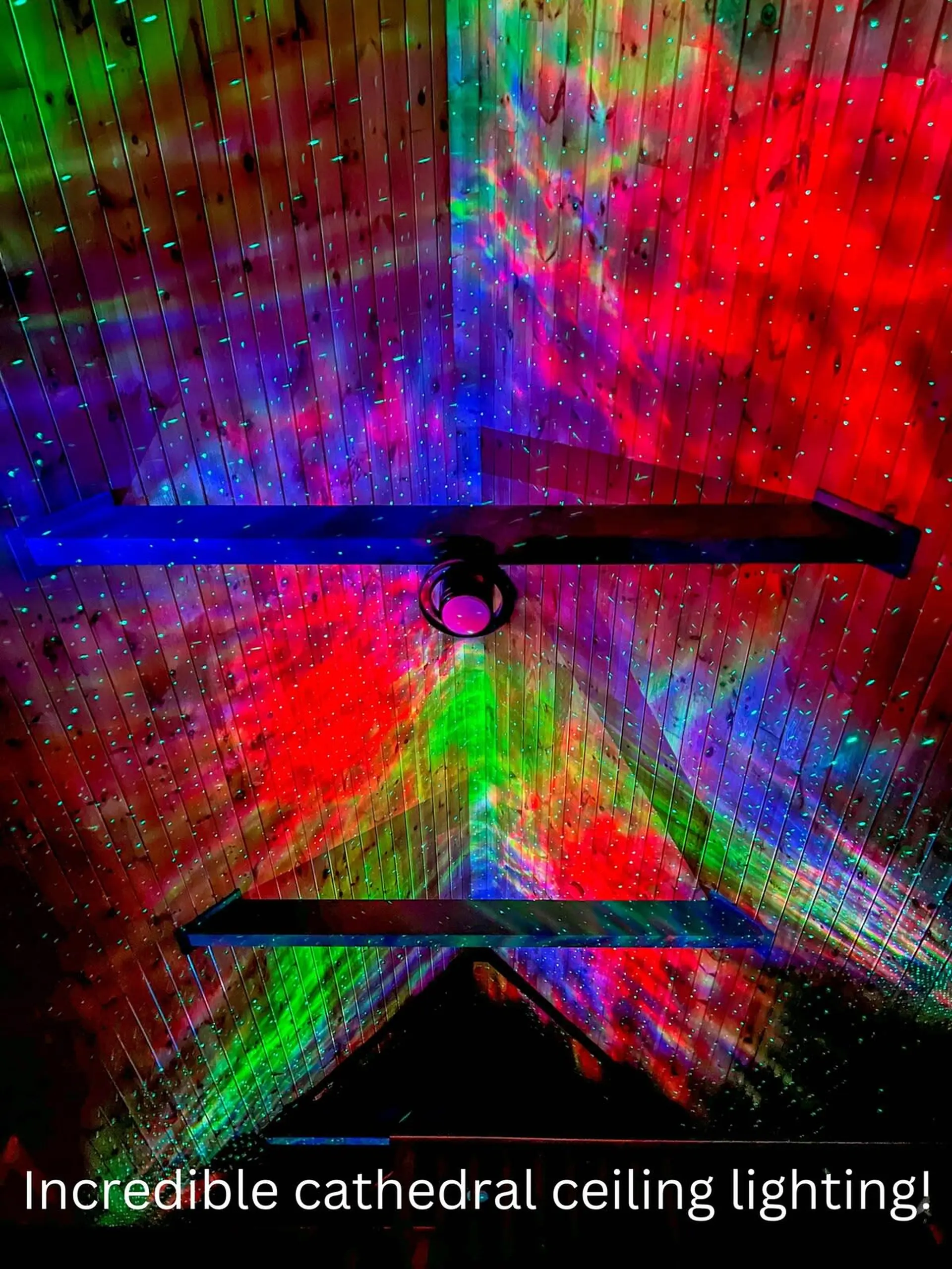 Vibrant lights project colorful patterns and stars onto a wooden cathedral ceiling.