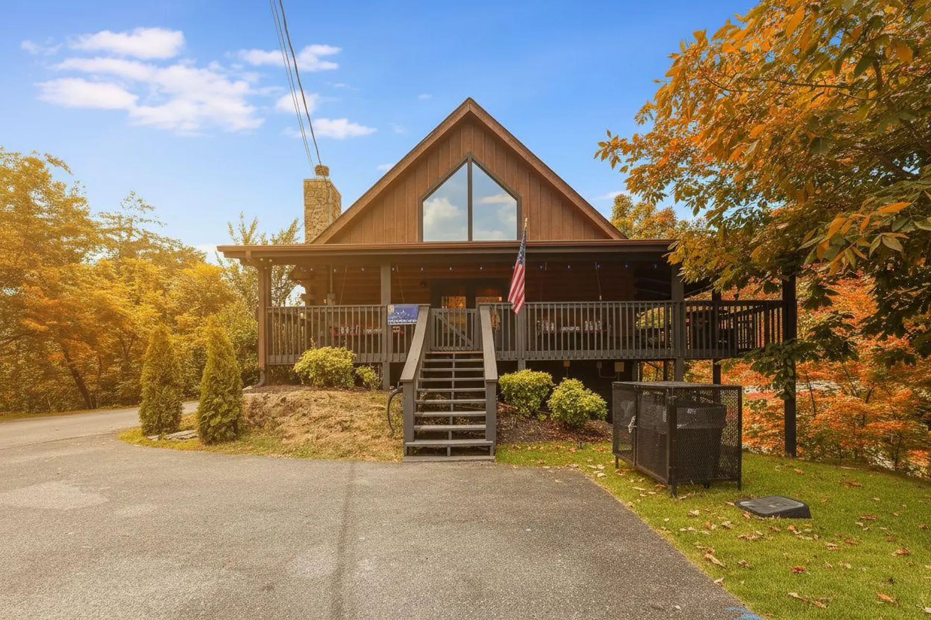A cozy wooden cabin with a large front porch and an American flag, surrounded by vibrant autumn foli