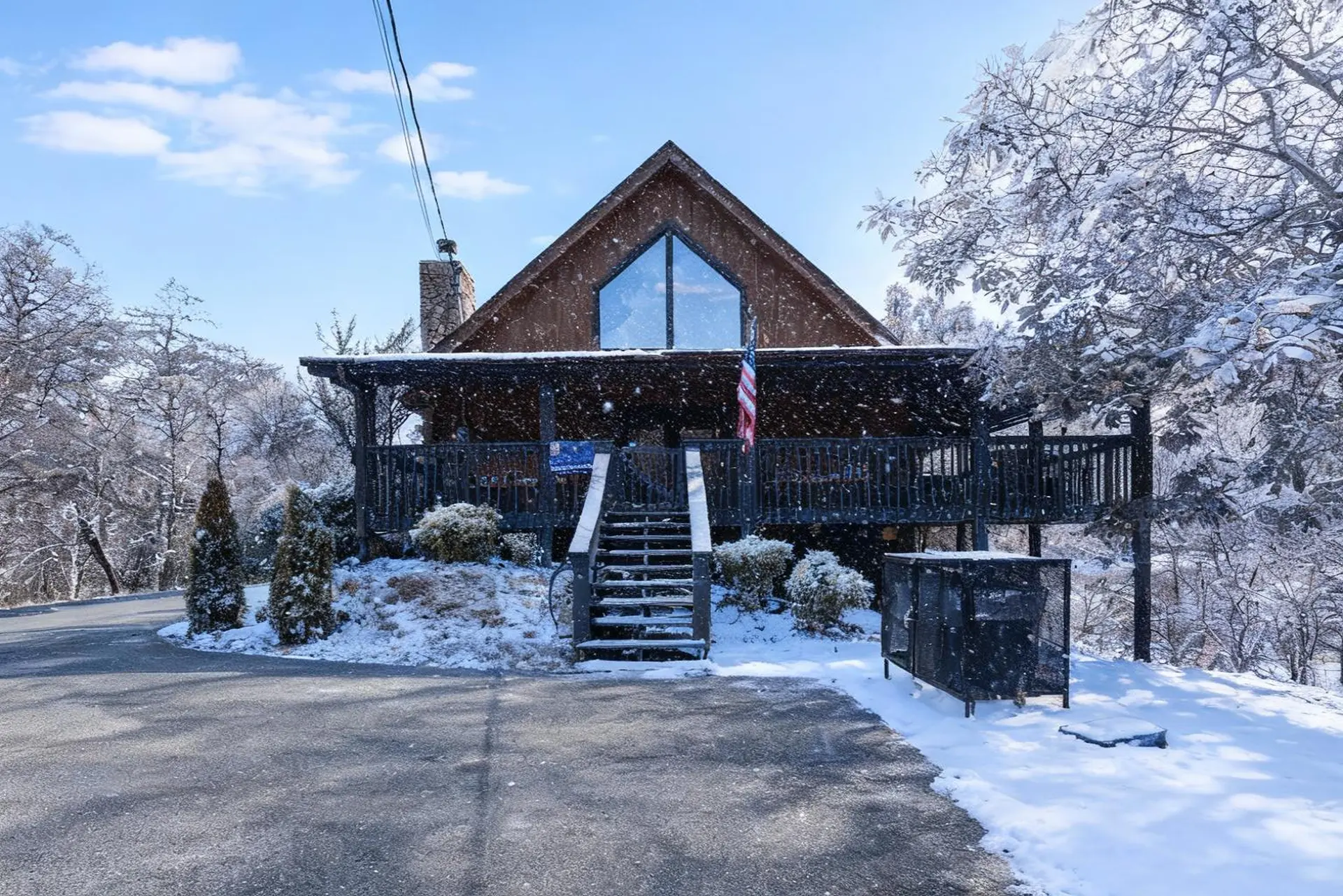 A snow-covered cabin with a large window, deck, and stone chimney.