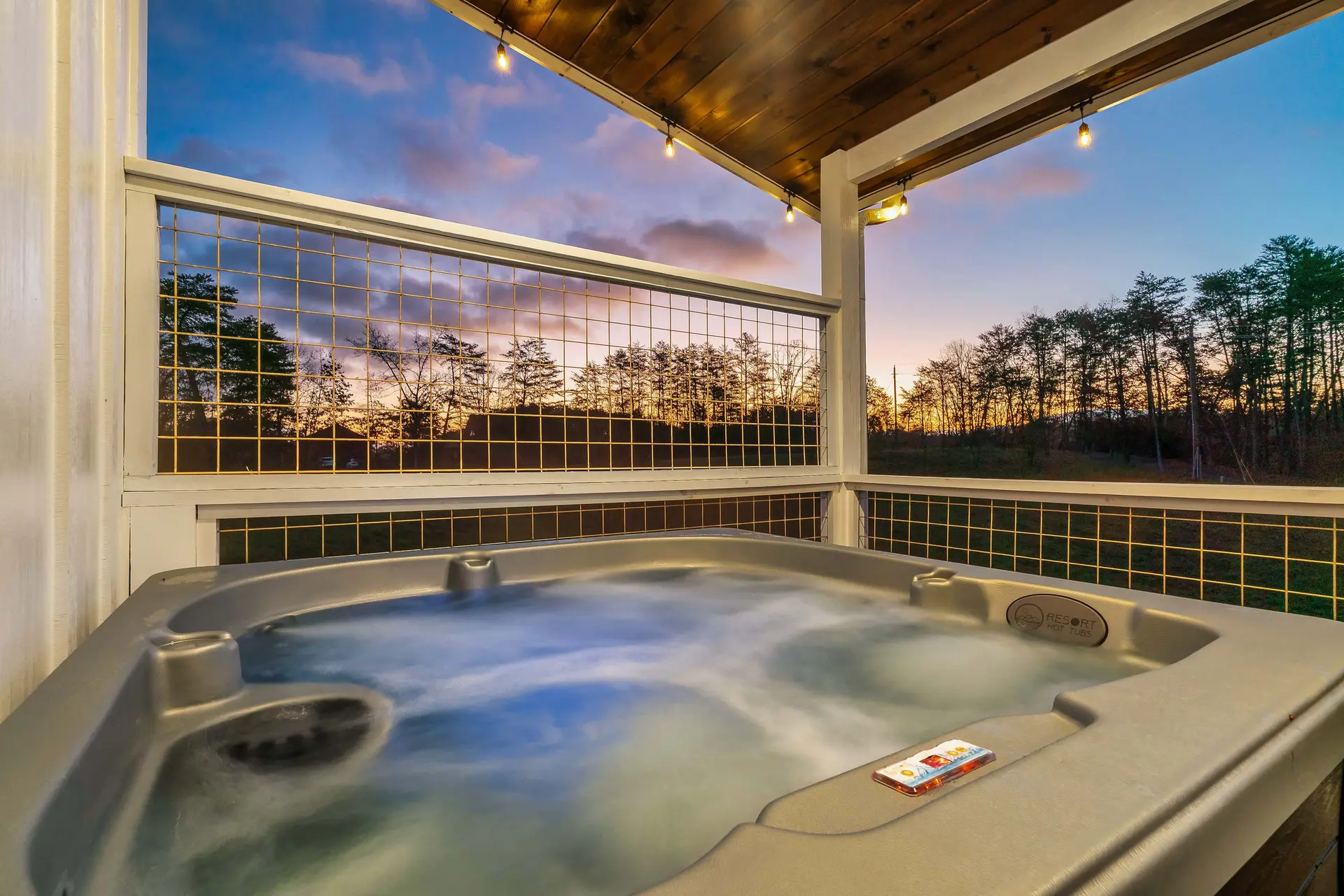 A hot tub sits on a deck at sunset, surrounded by trees.