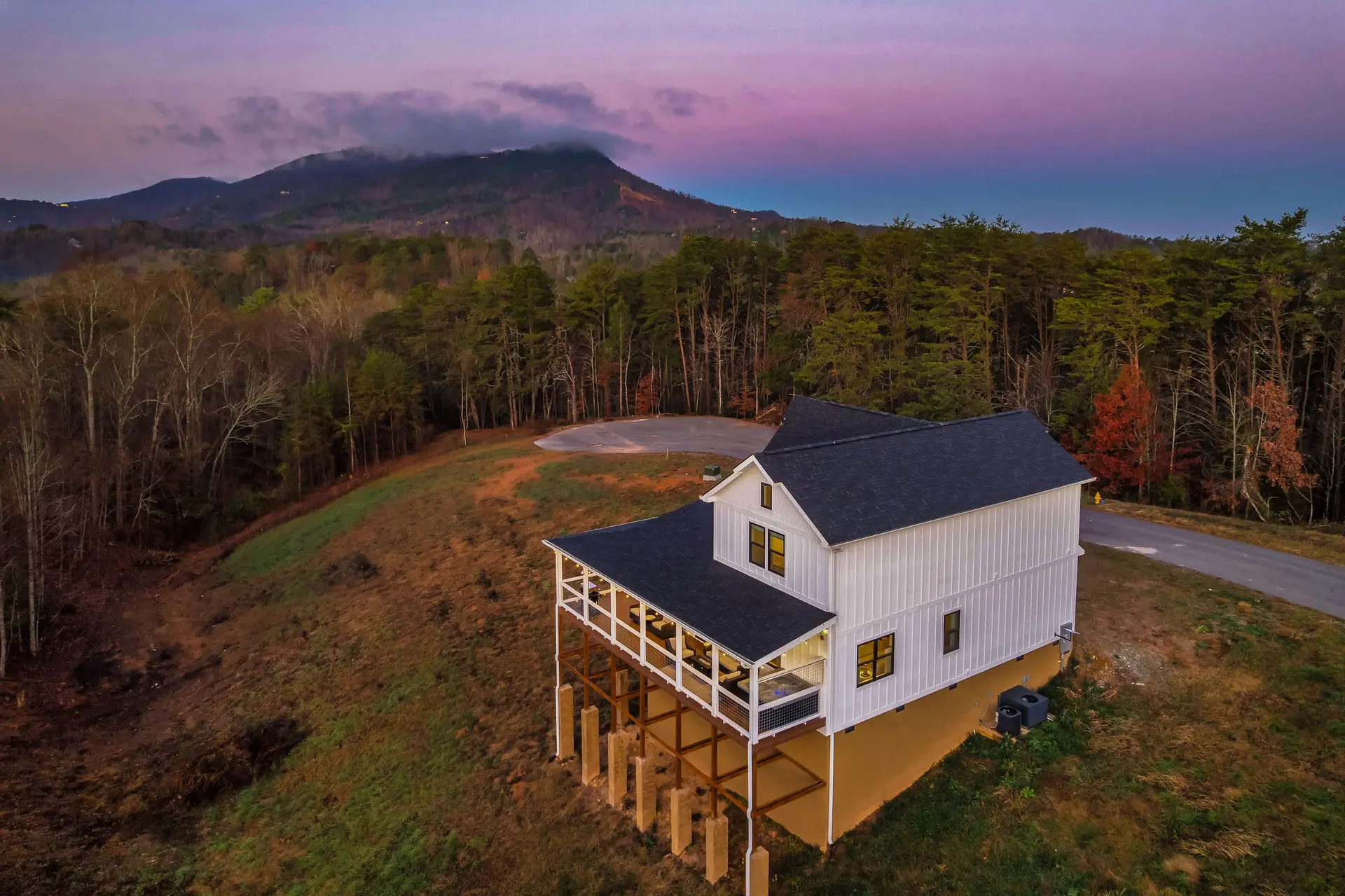 A white house with a dark roof sits on a hill overlooking a mountain range at dusk.