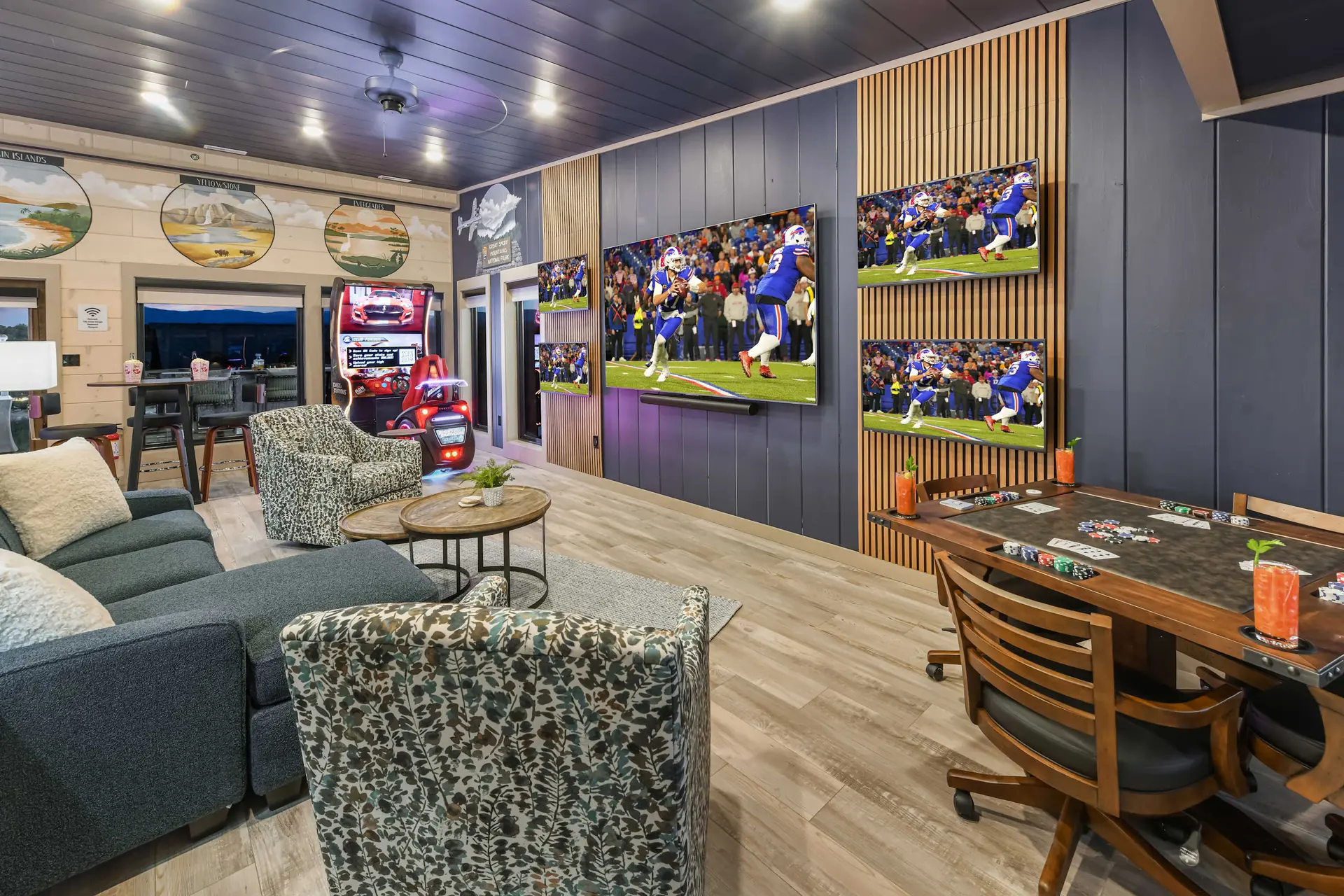 A game room with multiple TVs showing football, a poker table, arcade games, and comfortable seating