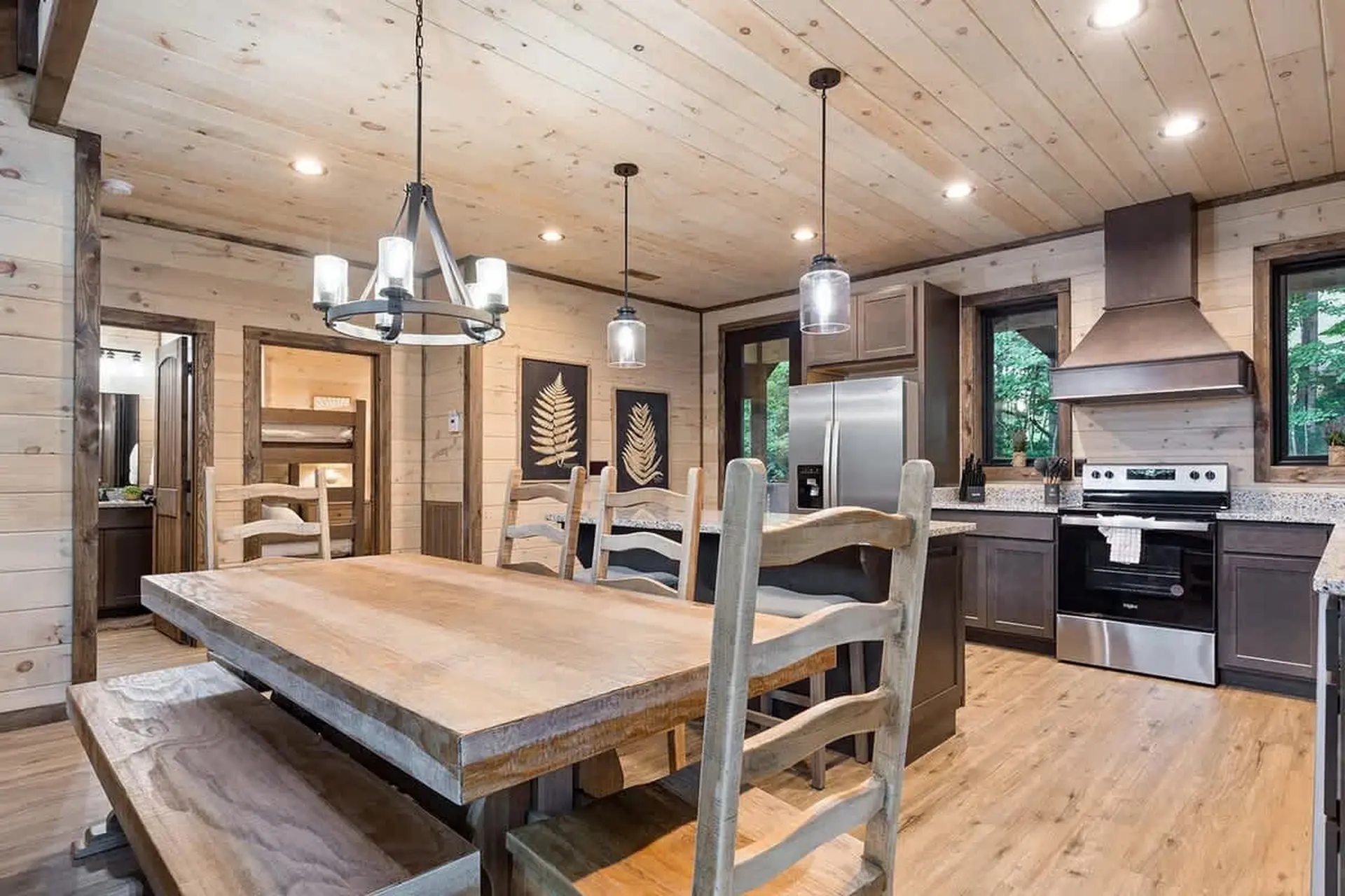 A dining room with a large wooden table and chairs, a kitchen with stainless steel appliances, and b