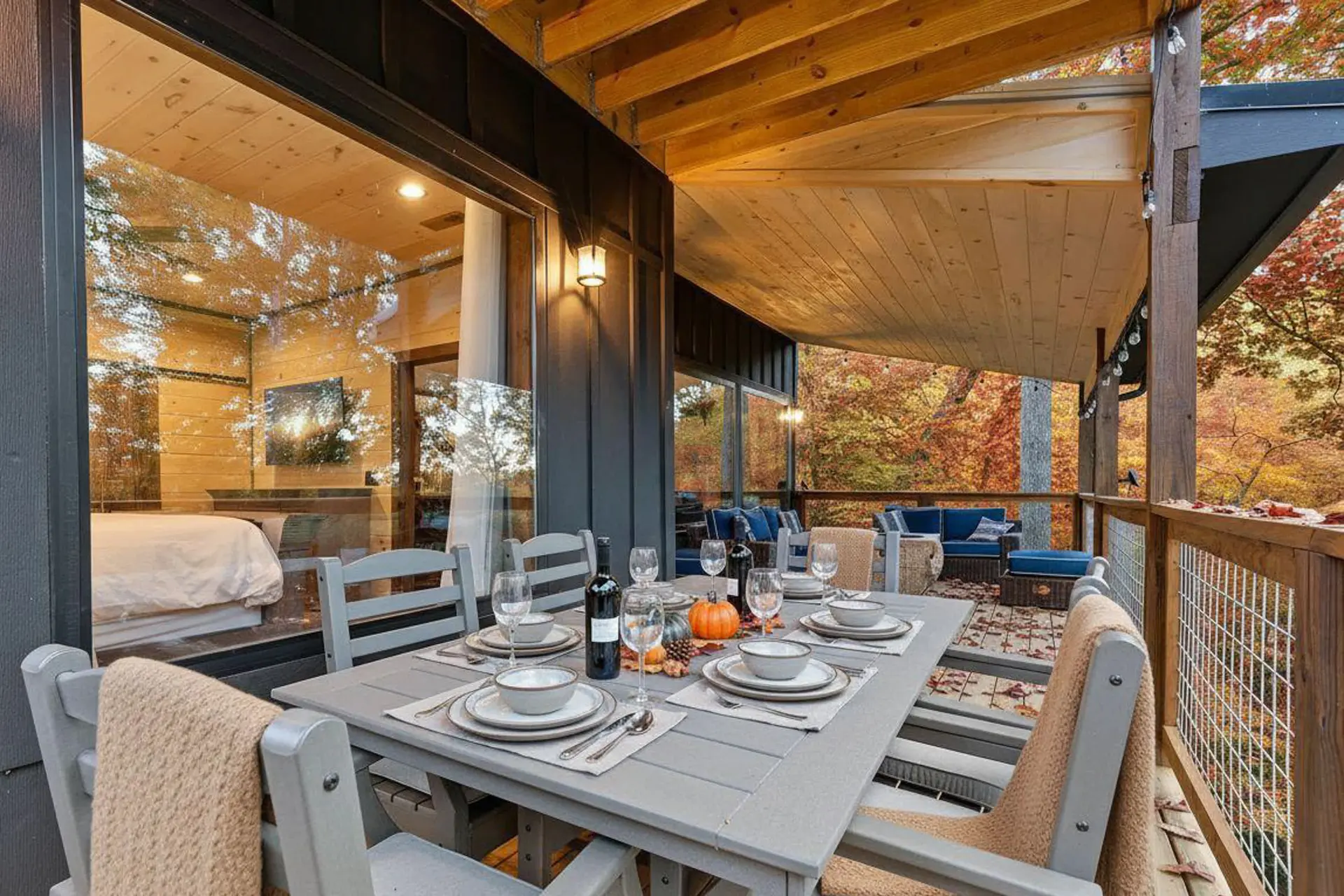 An outdoor dining table is set for autumn on a covered porch with fall foliage.