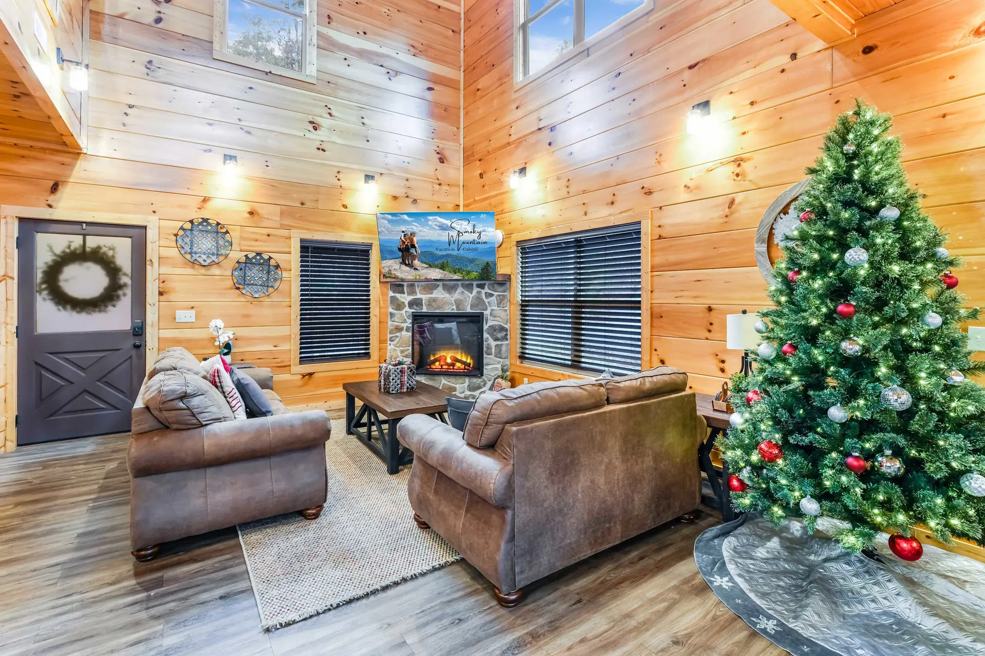 Cozy log cabin living room with fireplace, Christmas tree, and leather couches.