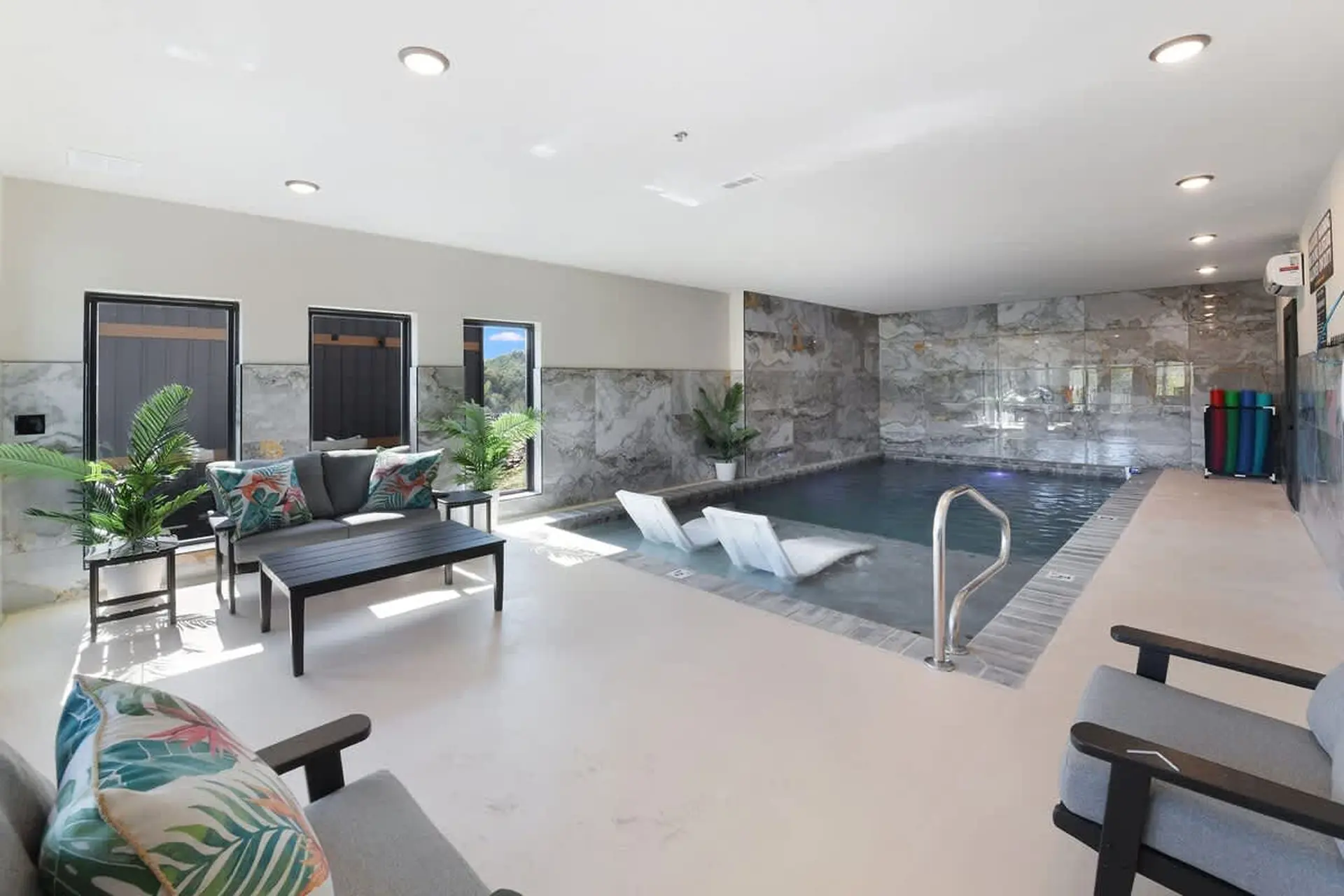 Indoor swimming pool with lounge chairs and seating area.