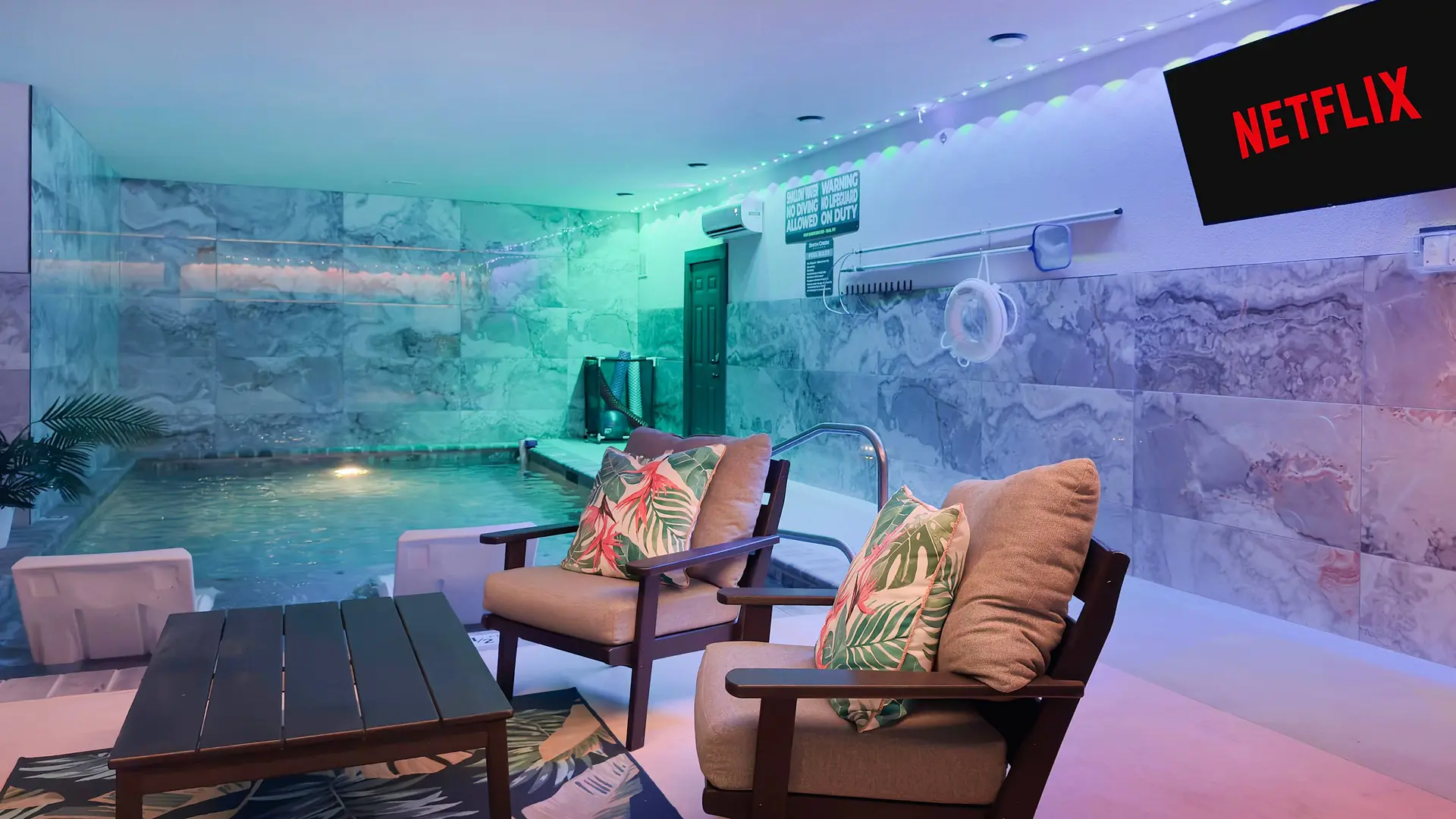 A dimly lit room with a pool, chairs, and a Netflix screen.