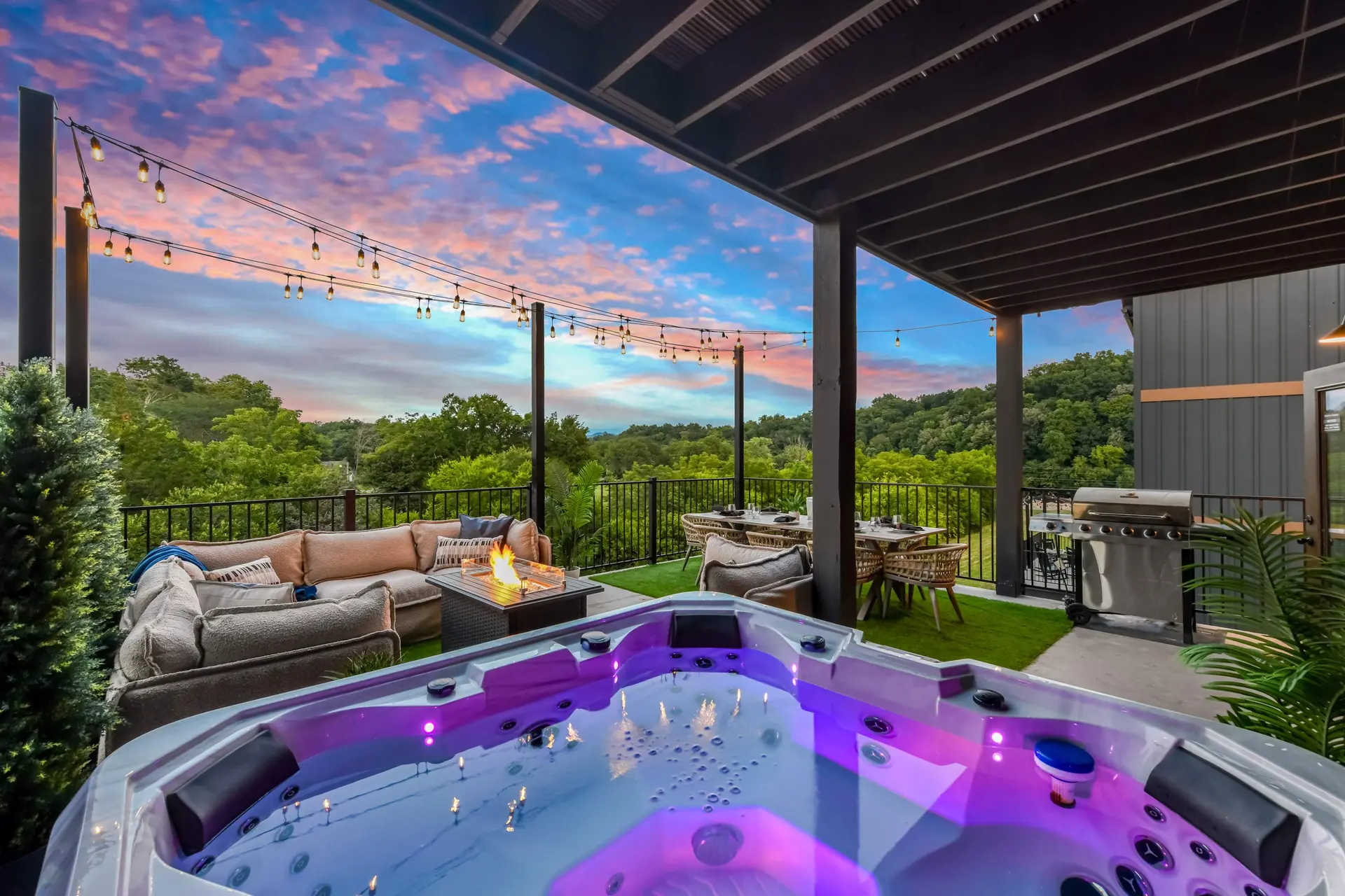 Outdoor deck with a hot tub, fire pit, seating, dining table, and grill at sunset.
