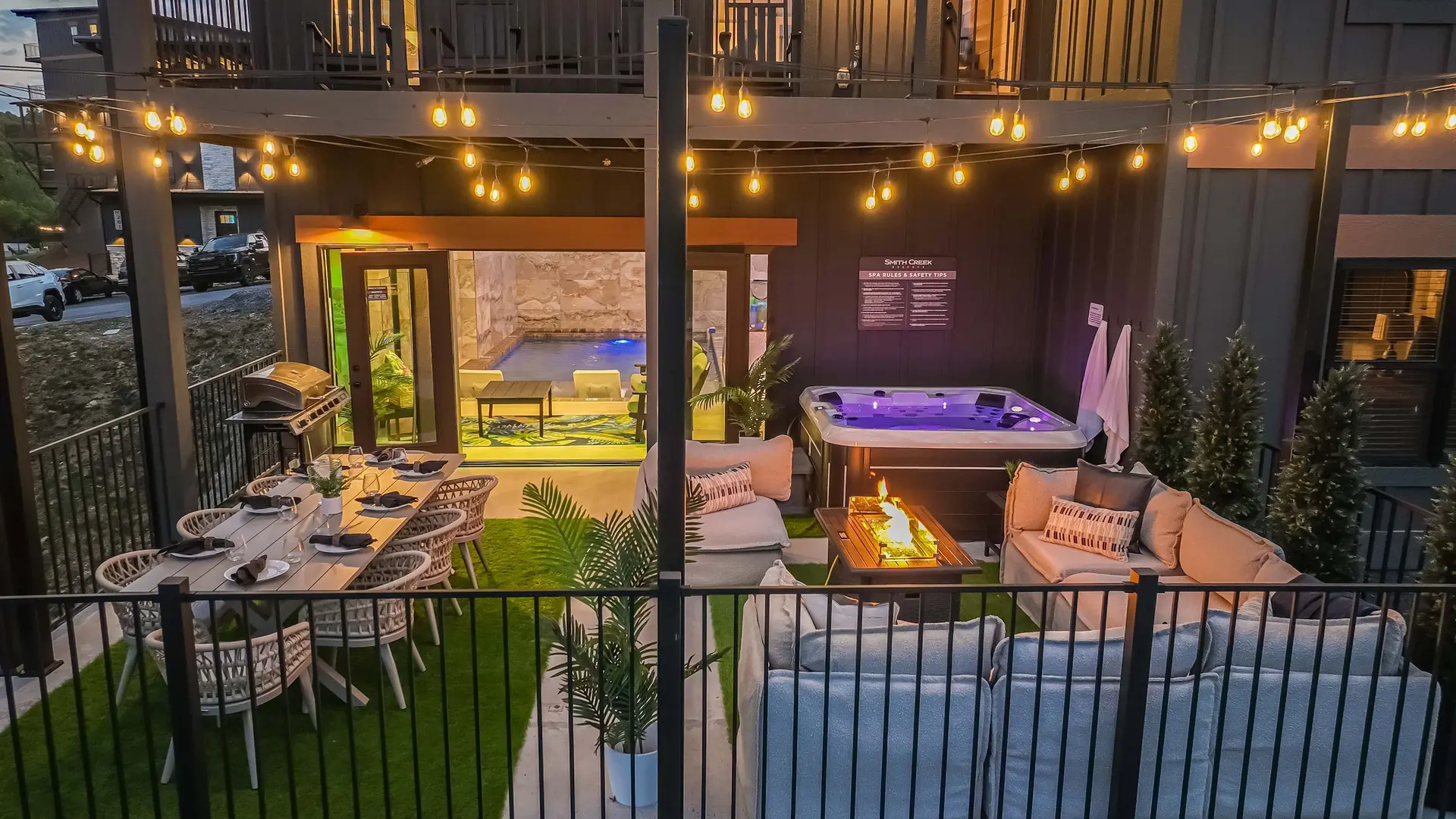 Outdoor patio with a dining table, hot tub, fire pit, and string lights.