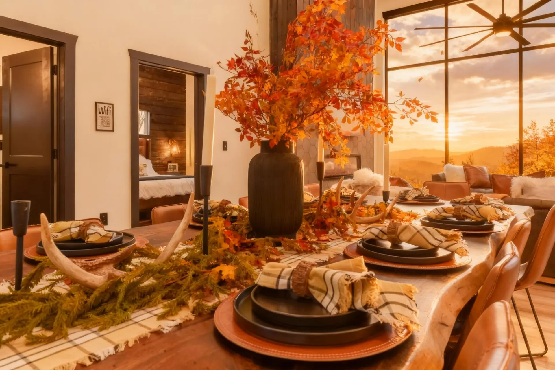 A dining table set for autumn with orange leaves, antlers, and a sunset view.