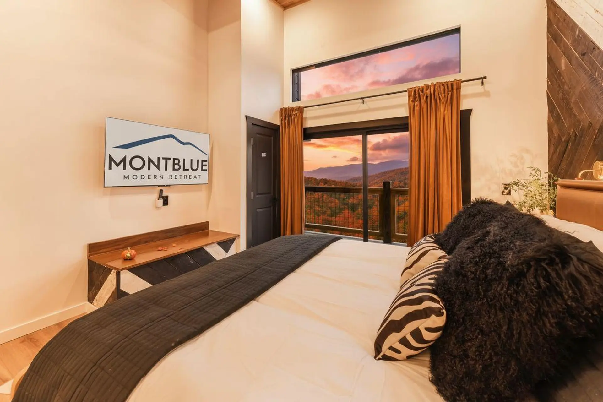 Bedroom with a large window overlooking mountains during sunset.