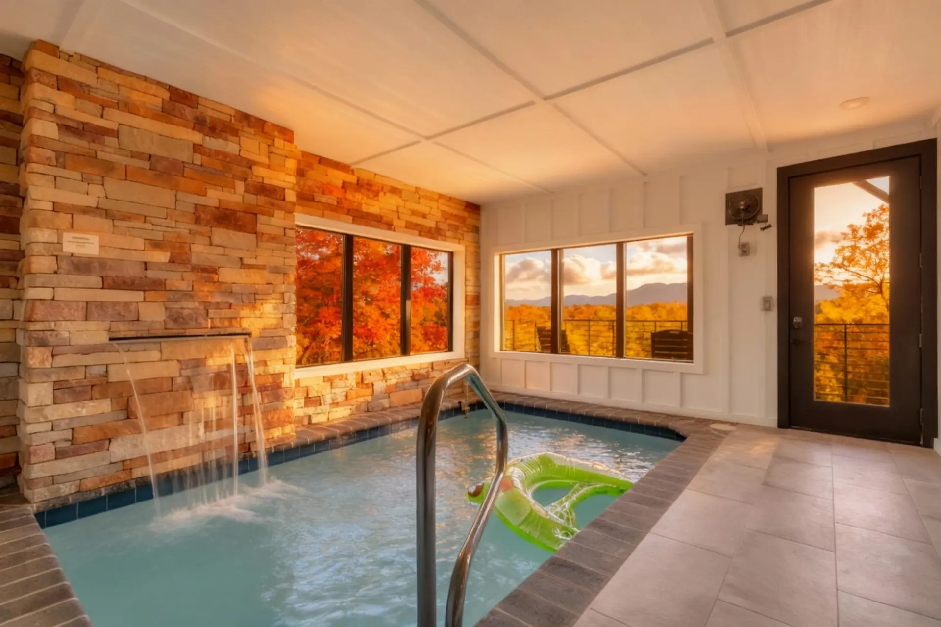 Cozy indoor jacuzzi with a waterfall, surrounded by fall foliage views.